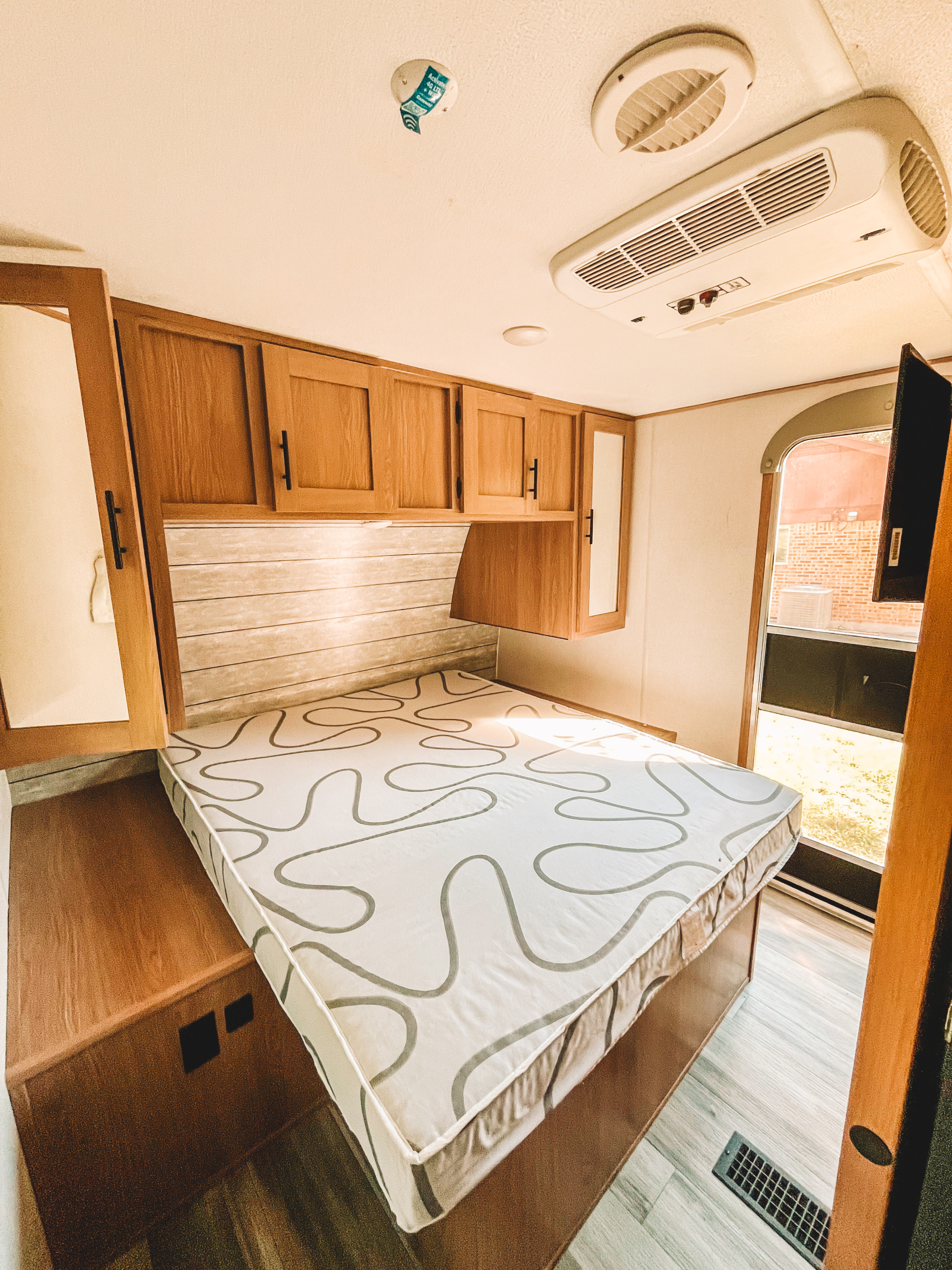 Inside a cozy RV rental: a bright bedroom with a patterned mattress, wooden cabinets, and AC. Perfect for your travels!. Forest River PrimeTime Avenger 2023