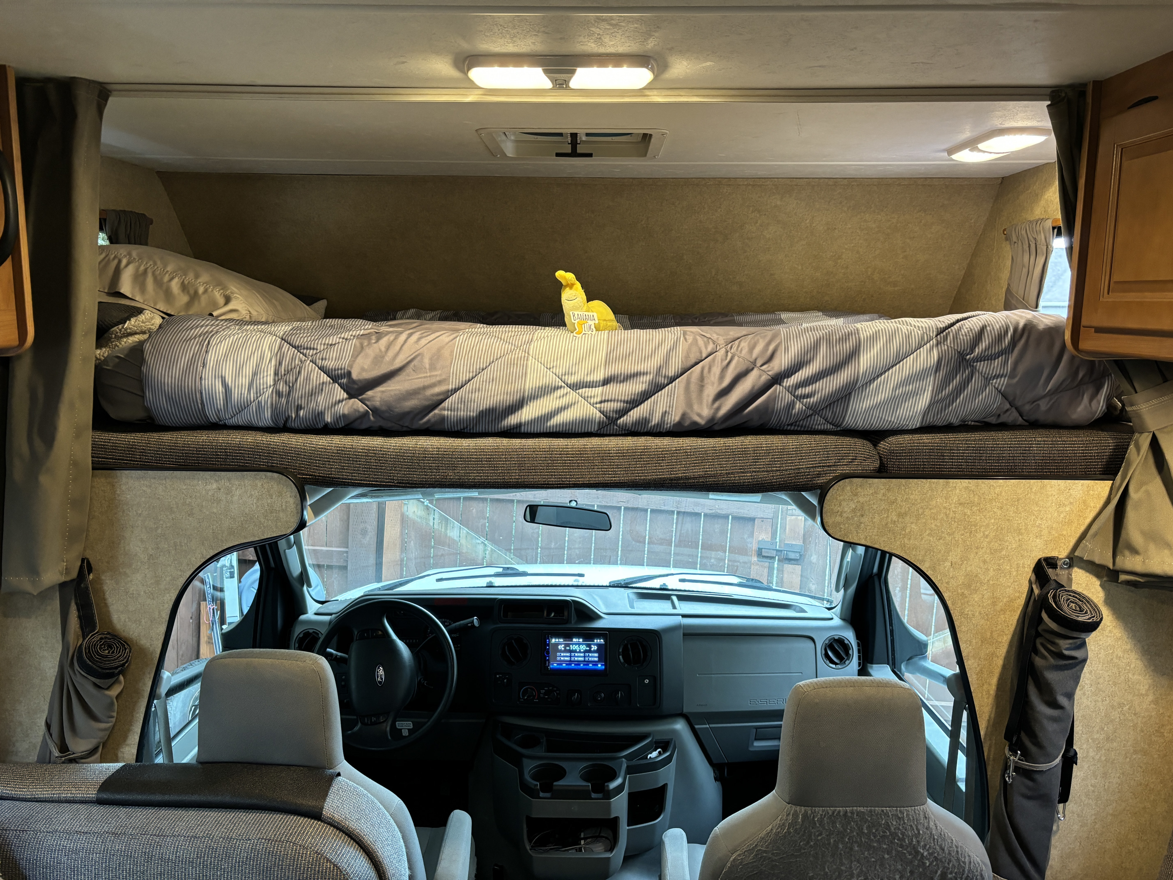 Inside an RV rental: View from the living area showing the front cockpit and an overhead cab-over bed with bedding.. Thor Majestic 2015