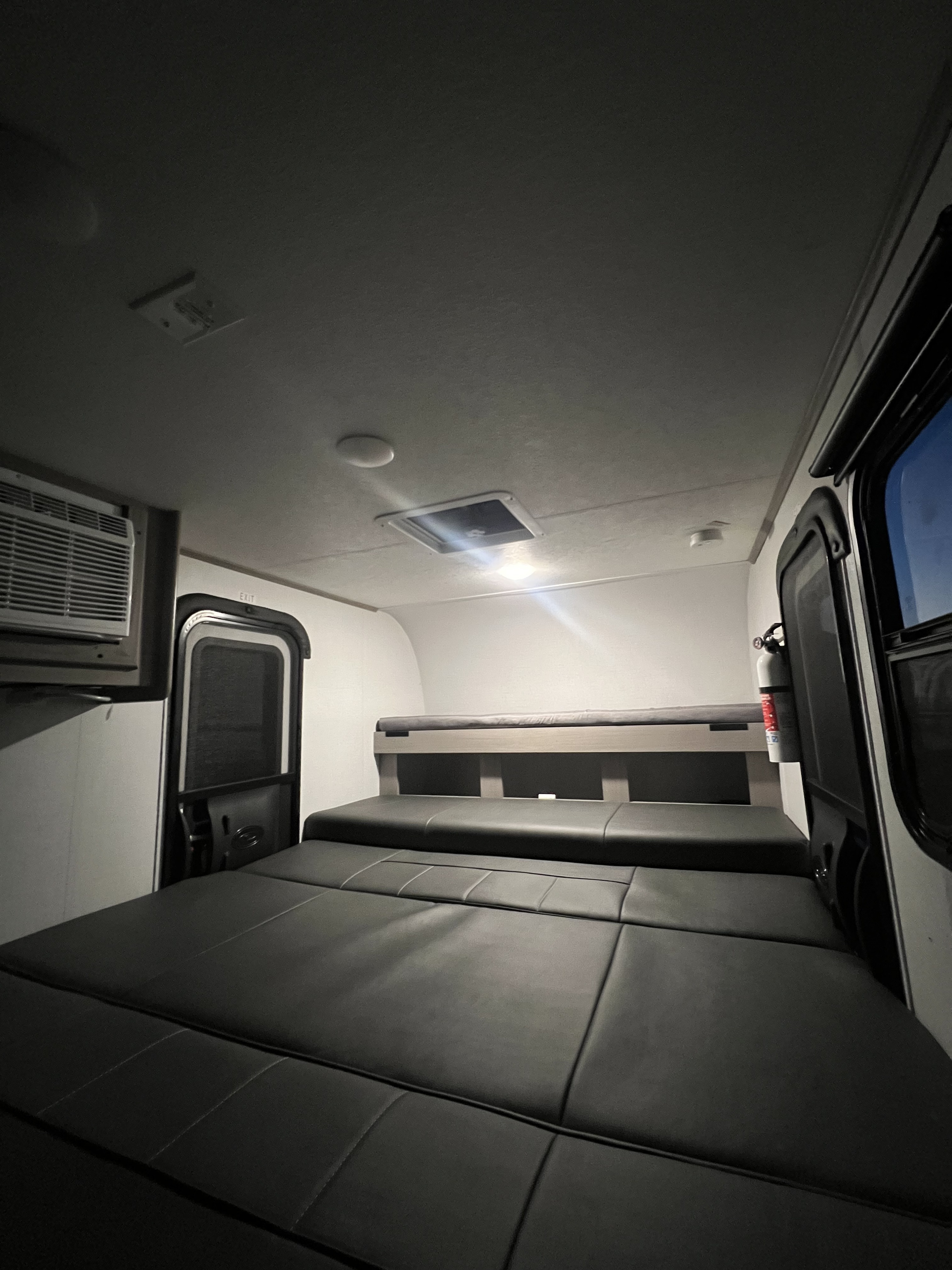 Inside an RV rental: a cozy sleeping area with convertible seating, a top bunk, AC unit, and fire extinguisher, ready for your trip.. Dutchmen Rubicon 1400 BH 2024