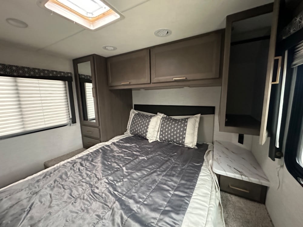 Spacious RV rental bedroom featuring a comfy bed, overhead cabinets, and a side table with marble top.. Thor Freedom Elite 2024