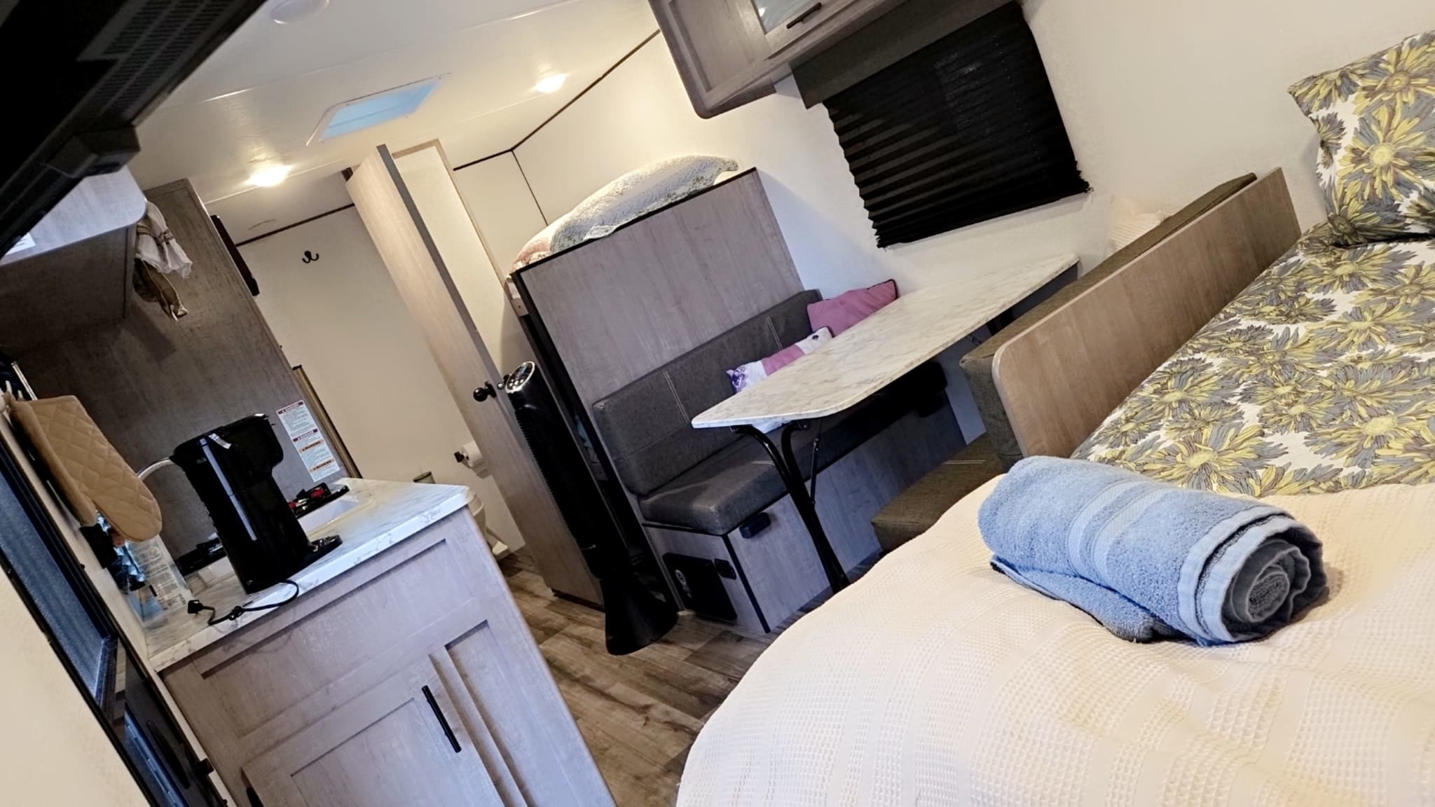This inviting RV rental interior showcases a cozy bed, a practical dining dinette, and a compact kitchen setup.. Coleman 17B 2024