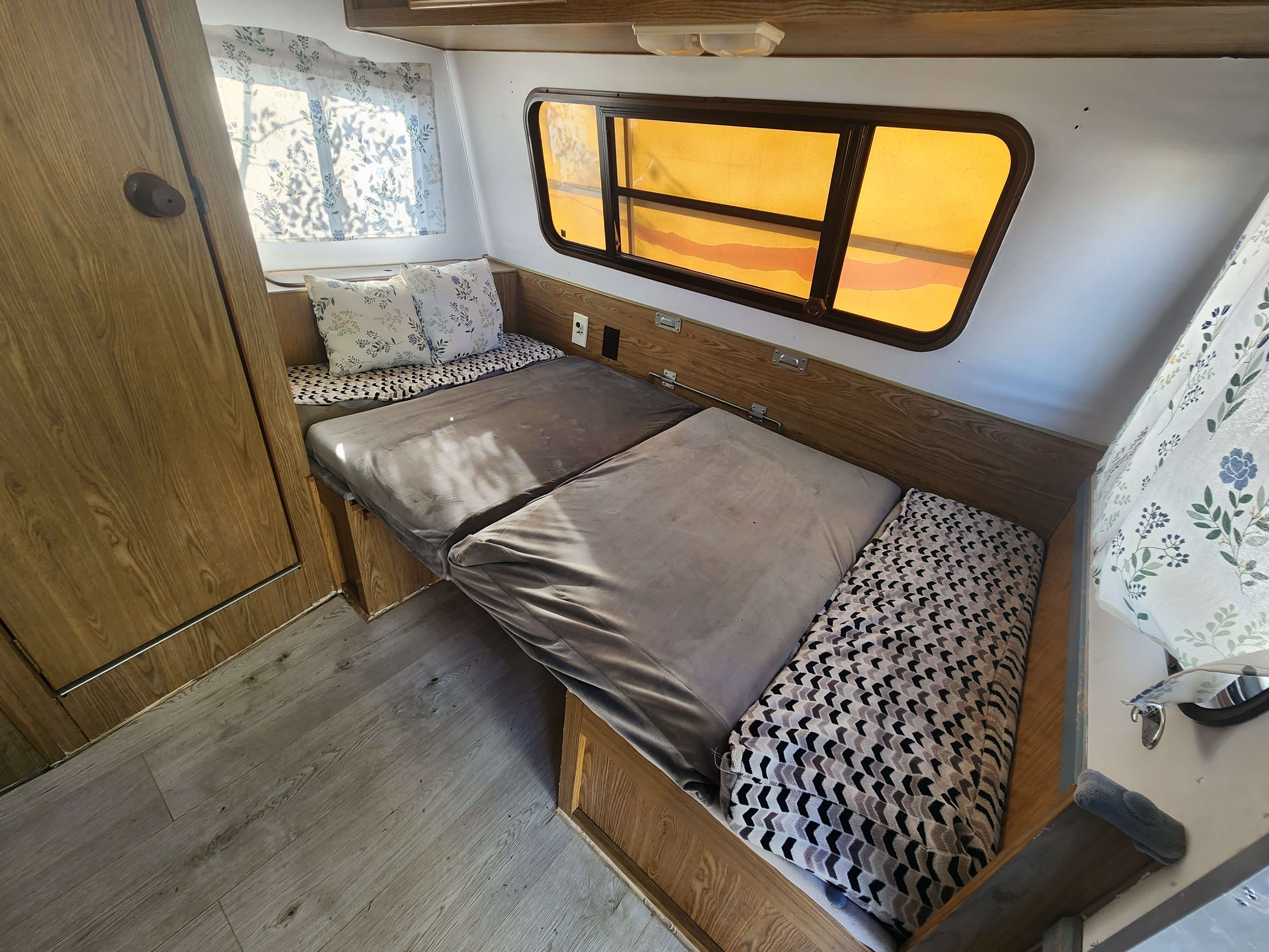 Cozy RV rental interior featuring a bed with patterned cushions, wooden walls, and windows with amber shades.. Fleetwood Wilderness 1991