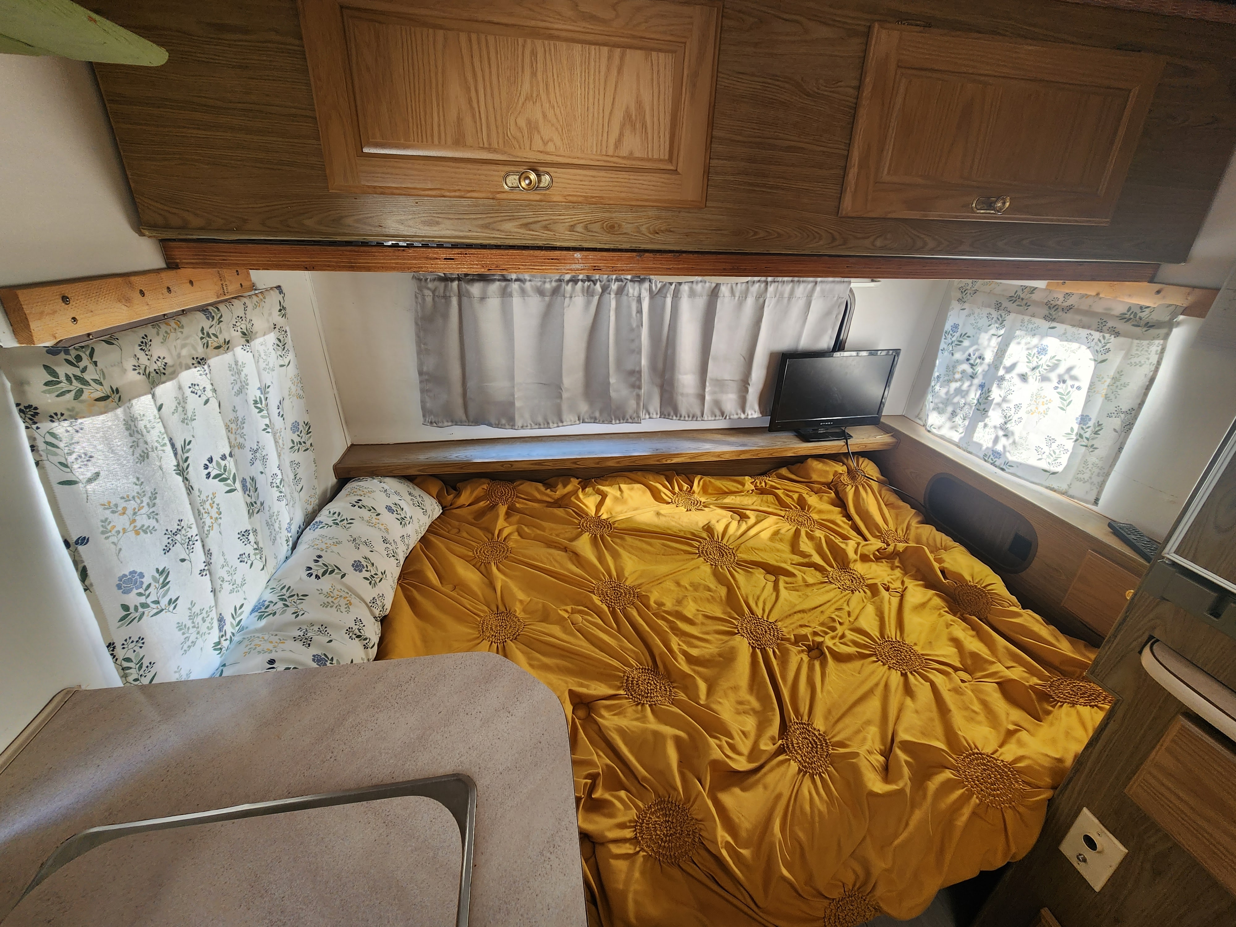 Inside an RV rental: a cozy bedroom with a vibrant yellow bed, floral curtains, and TV for a comfortable stay.. Fleetwood Wilderness 1991