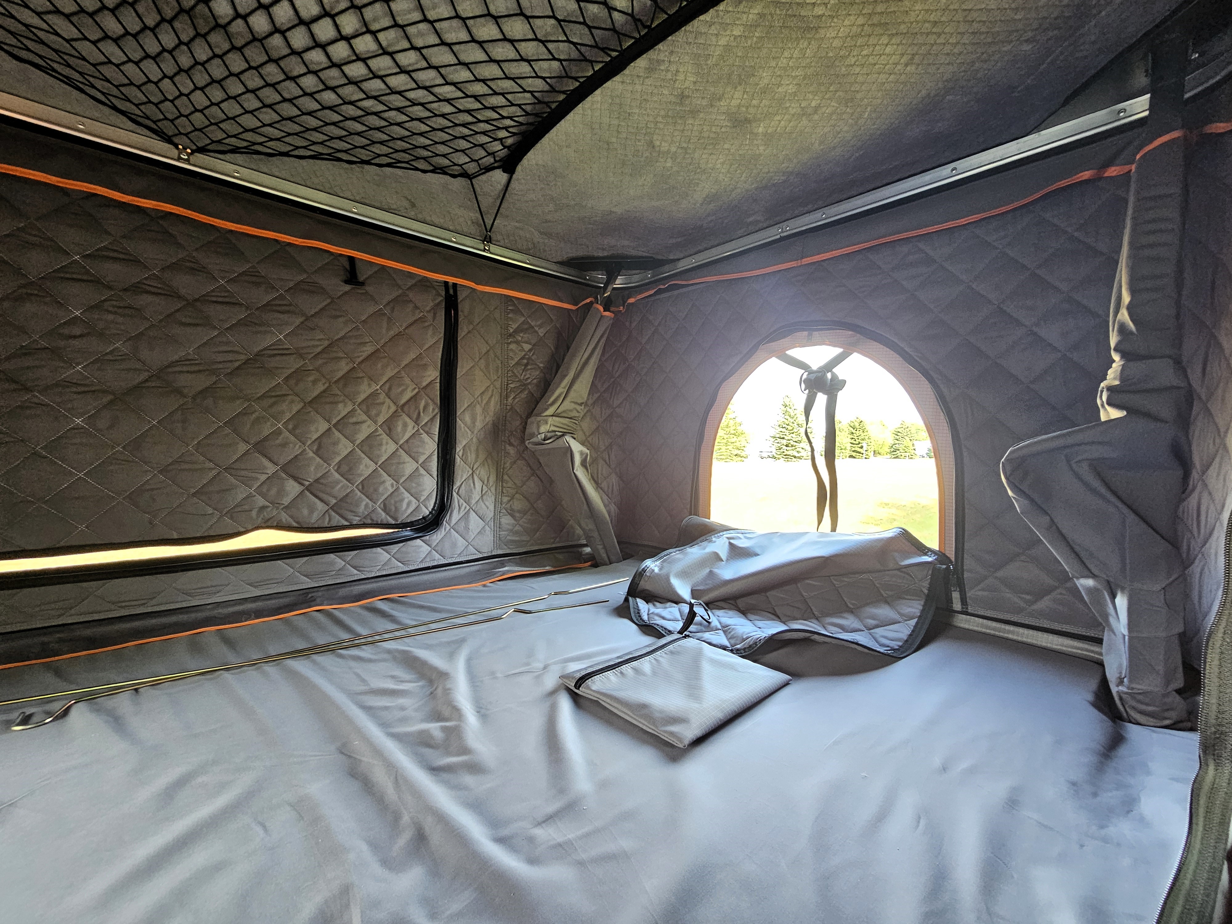 Experience a cozy RV rental: view inside a rooftop tent with quilted walls, comfy sleeping area, and ceiling net storage.. OTG Campers Voyager X 2024