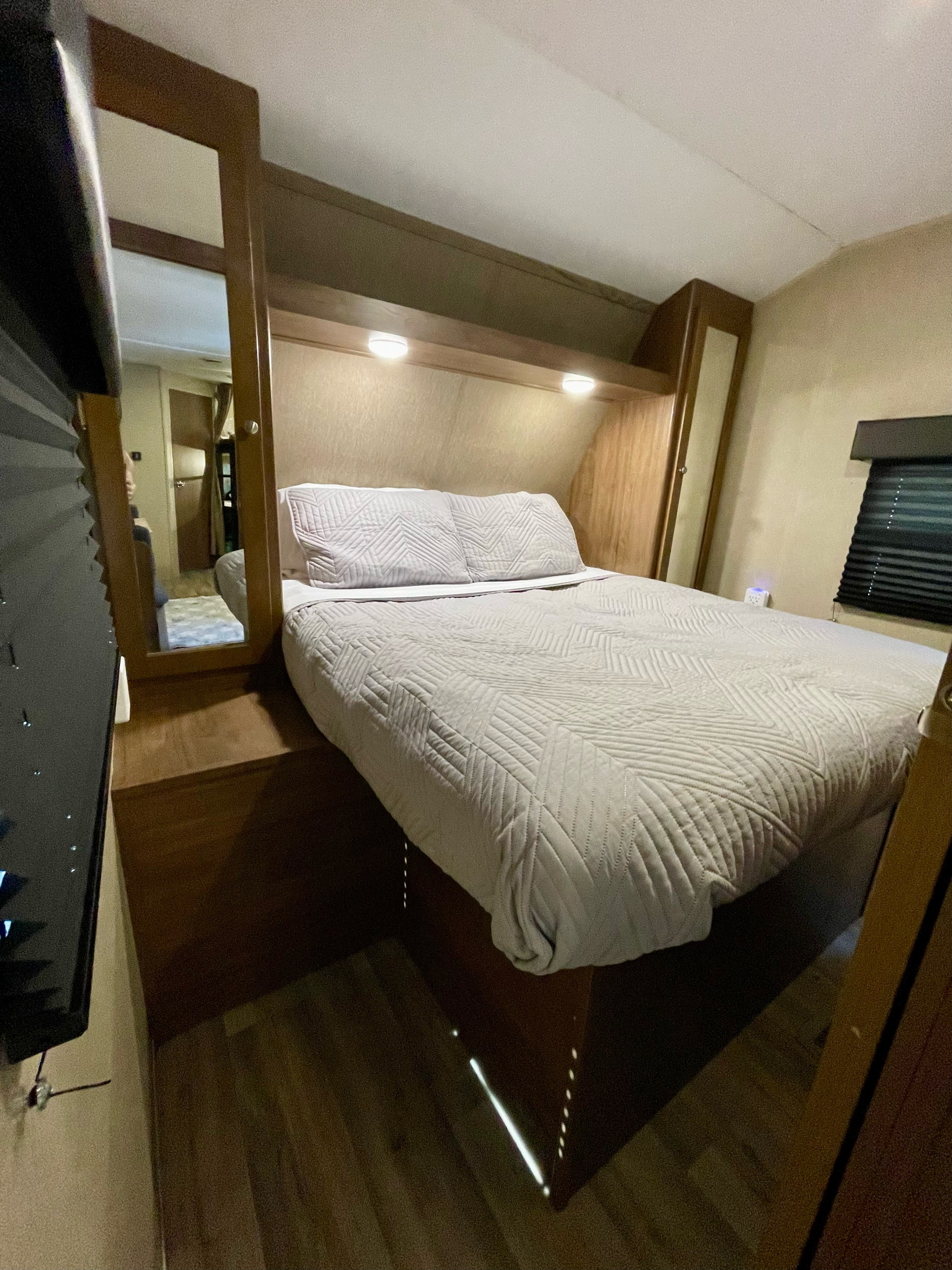 An inviting **rv rental** bedroom with a quilted bed, headboard lighting, and built-in mirror, offering compact comfort.. Dutchmen Aspen Trail 2017
