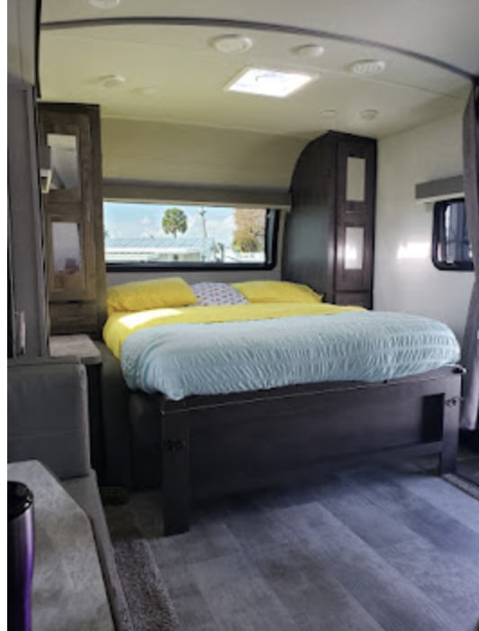 Inside an RV rental, a welcoming bedroom features a large bed, overhead storage, and a scenic window view.. Forest River Rockwood 2021