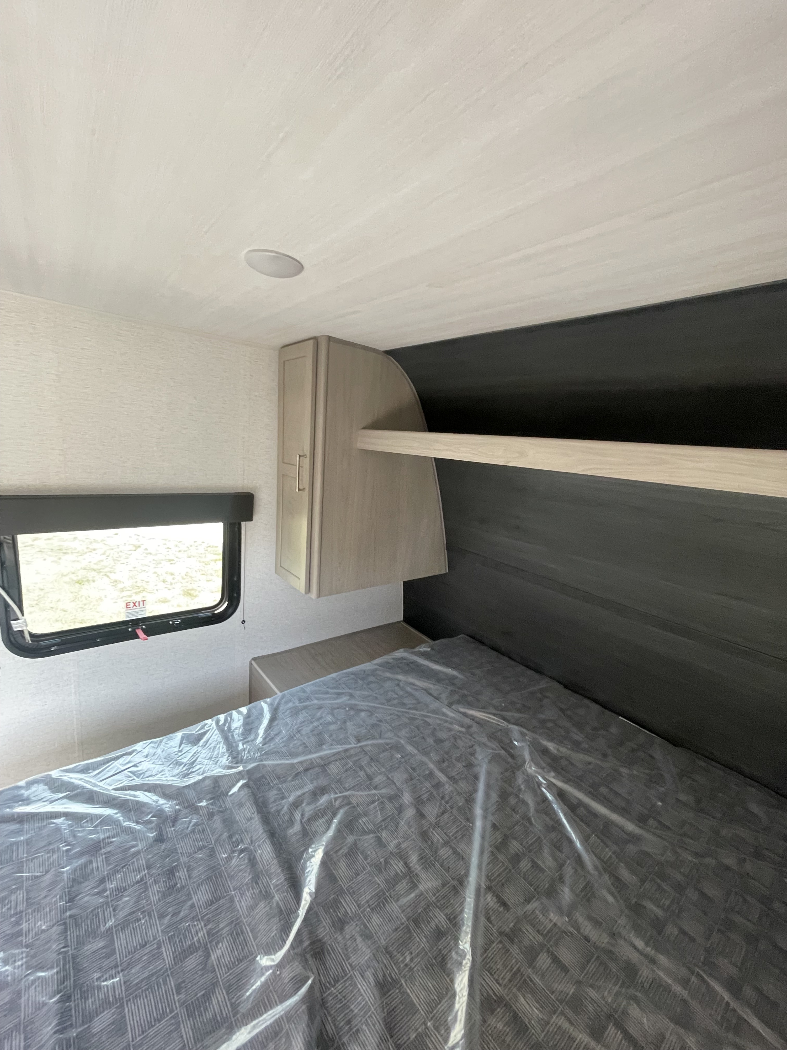 Compact RV rental bedroom interior with a plastic-covered bed, window, and built-in storage, ideal for travel.. Keystone RV Springdale 2024