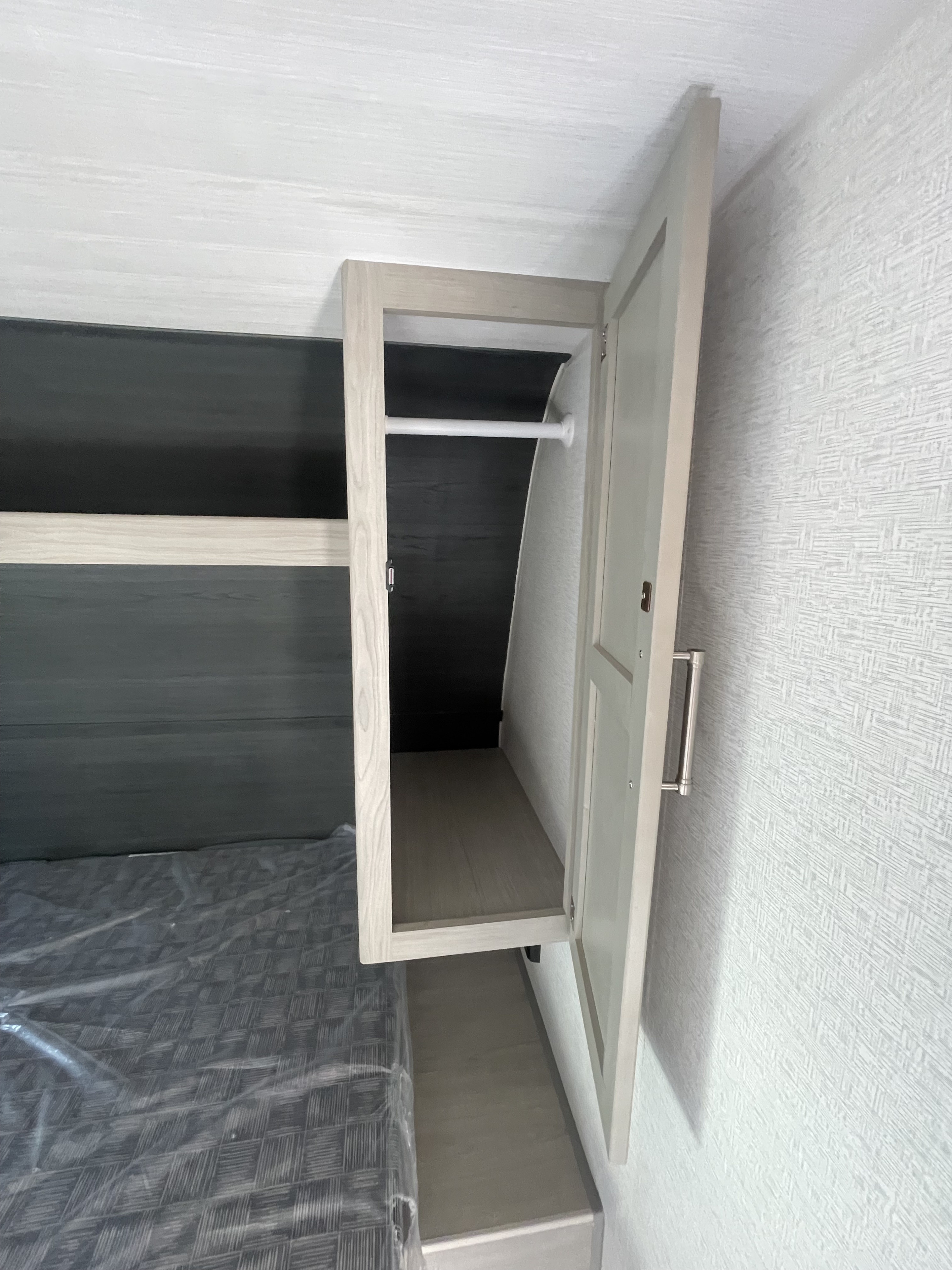 Inside an RV rental, showing an open wardrobe with a hanging rod above a bed, ready for your travel essentials.. Keystone RV Springdale 2024