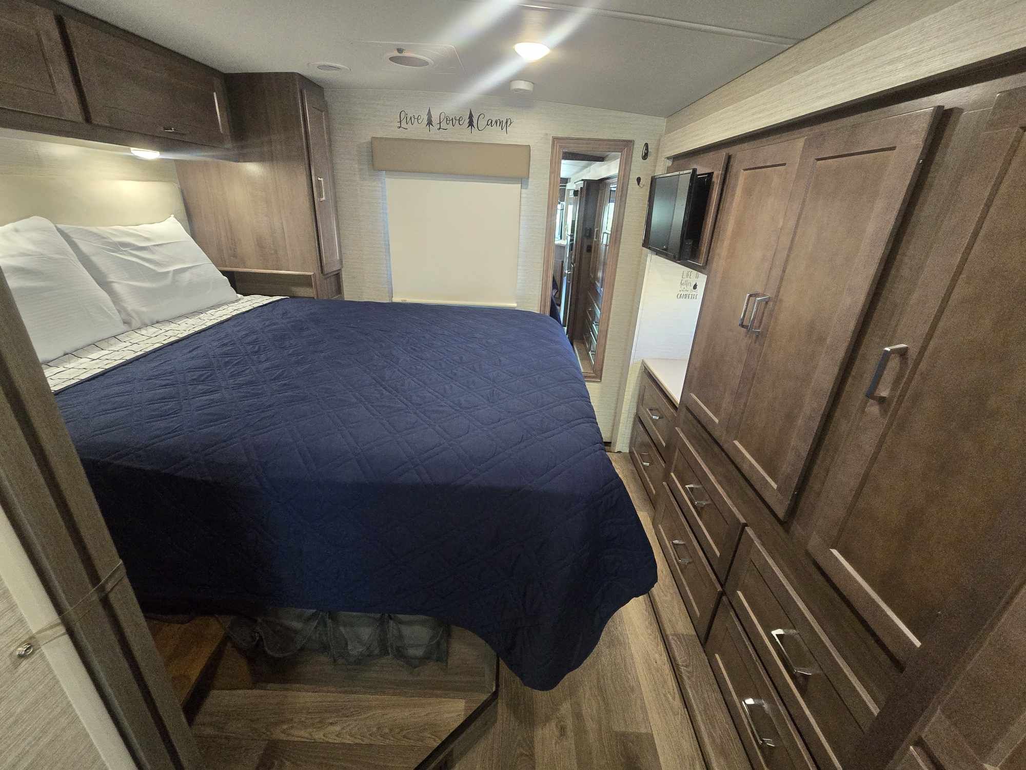 This RV rental bedroom offers a cozy bed, ample wood cabinetry, and TV, ideal for your next camping adventure.. Winnebago Sunstar 2022