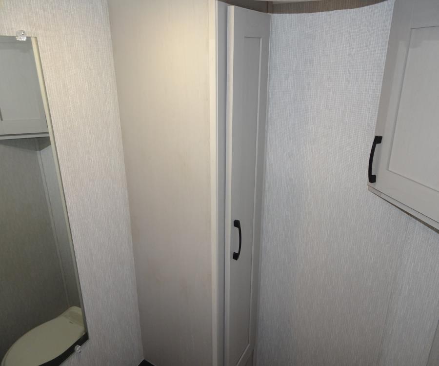 RV rental interior: compact bathroom with textured walls, reflected toilet, and light cabinets with black handles.. Coachmen Freelander 2023