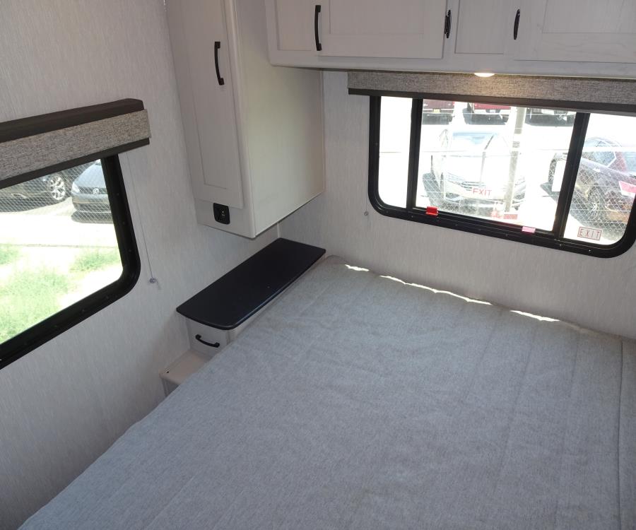 This RV rental bedroom features a compact sleeping area with a comfortable bed, storage cabinets, and bright windows.. Coachmen Freelander 2023