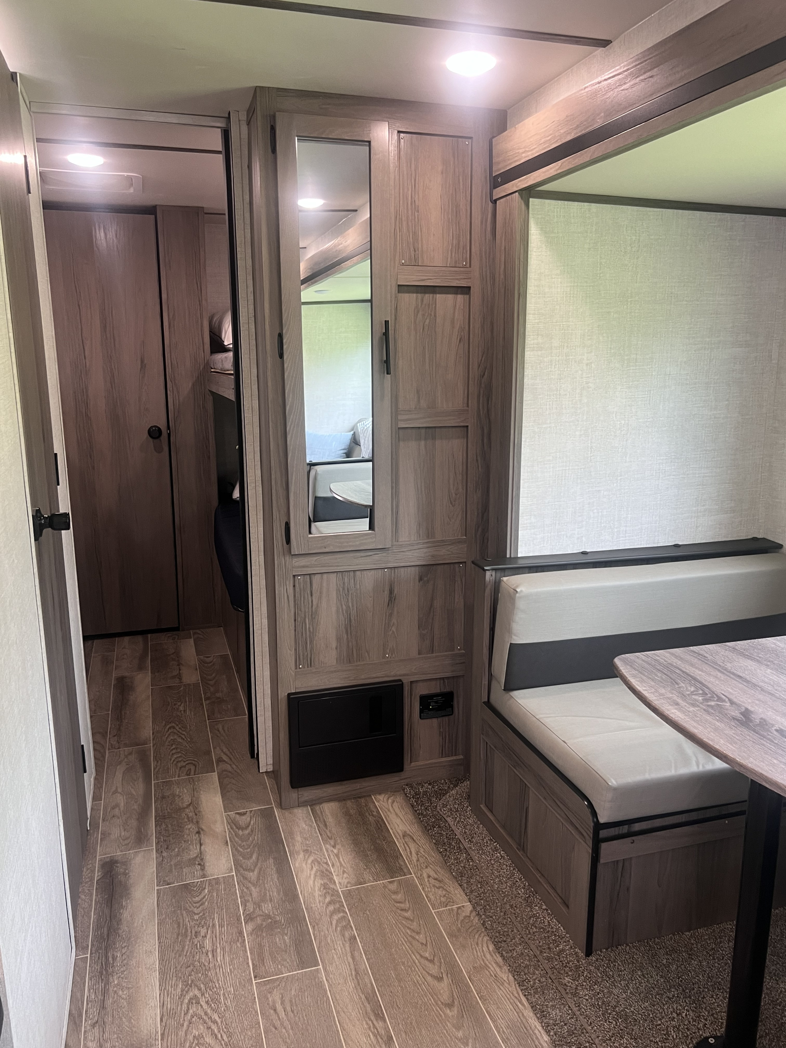 Inside an rv rental: light wood-look interior with a dinette booth, storage, a mirror, and wood plank flooring.. Gulf Stream Kingsport 2021