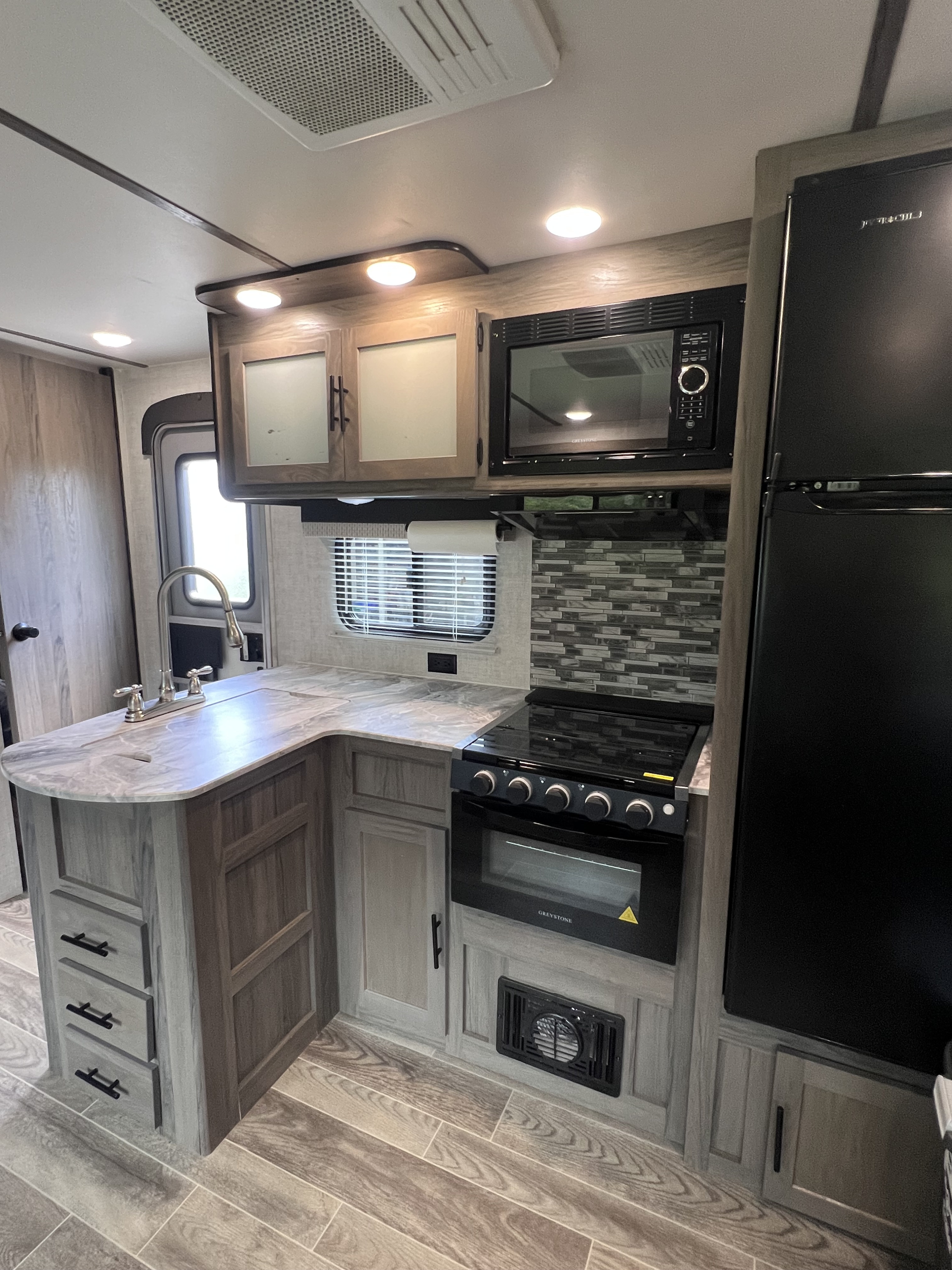 Modern RV rental kitchen with gray counters, black appliances, wood cabinets, and ample space.. Gulf Stream Kingsport 2021