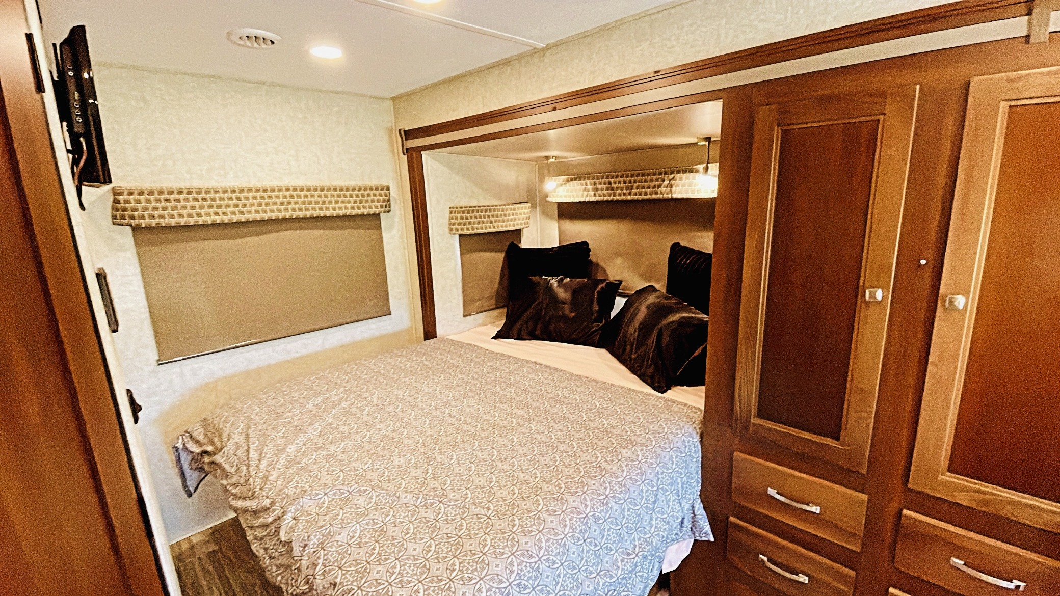 Cozy RV rental bedroom with a comfortable bed, integrated storage cabinets, a wall-mounted TV, and window blinds.. Forest River Sunseeker MBS 2019