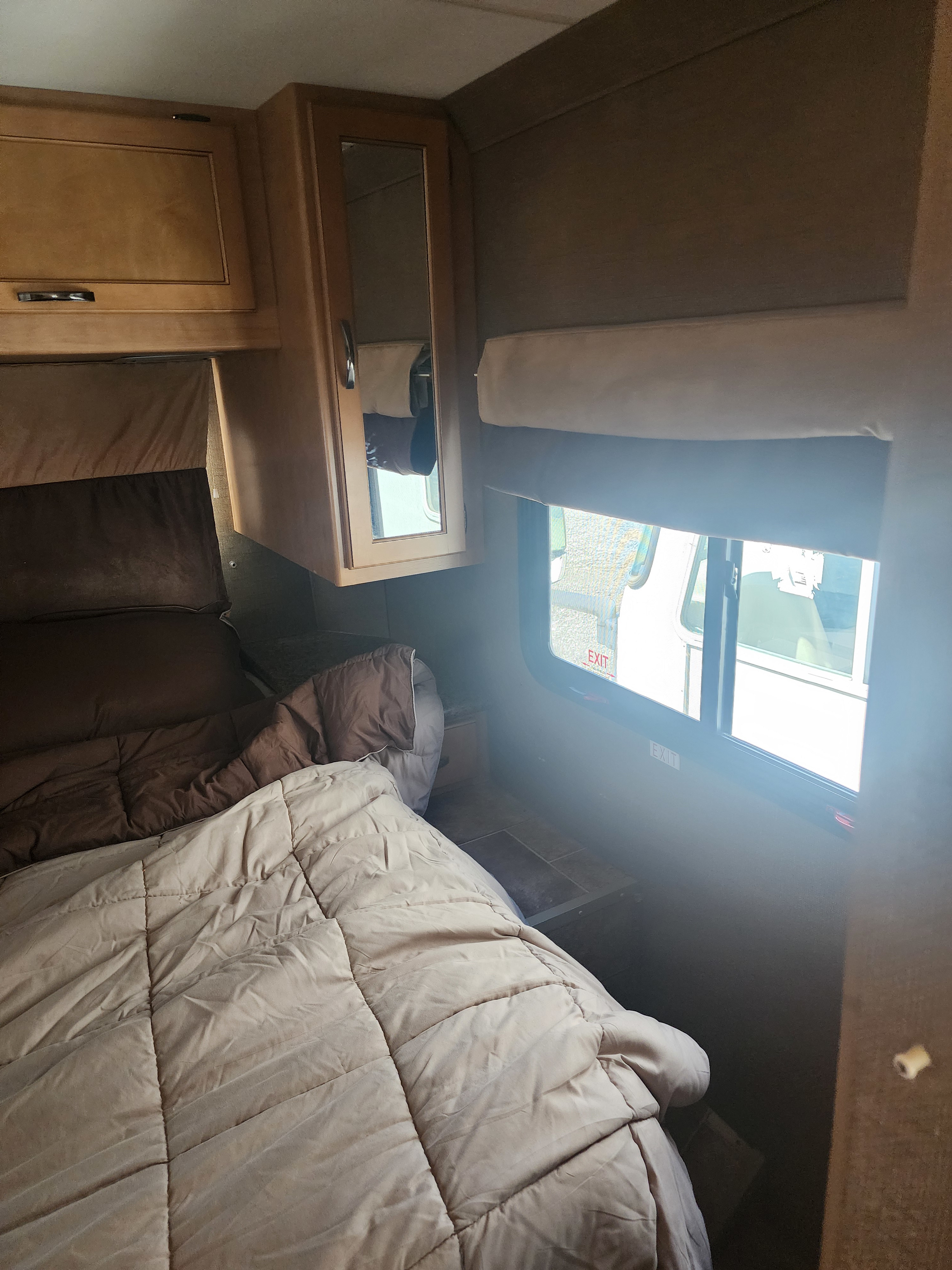 Cozy RV rental bedroom with wooden cabinets, a comfortable bed, and a window for natural light. Ideal for road trips.. Thor Motor Coach Four Winds 2015