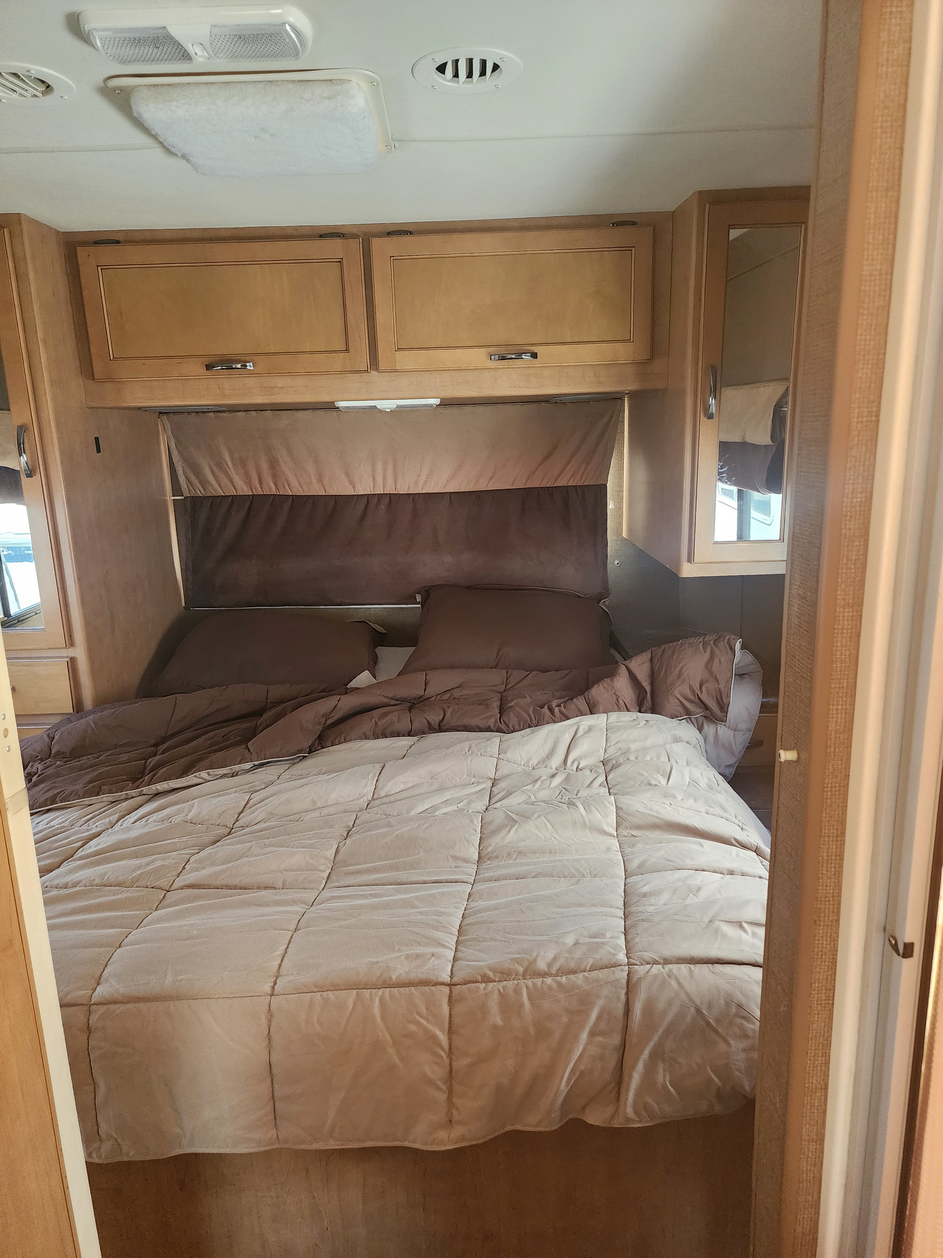 Comfortable RV rental bedroom with a cozy bed, natural wood cabinets, and functional lighting.. Thor Motor Coach Four Winds 2015
