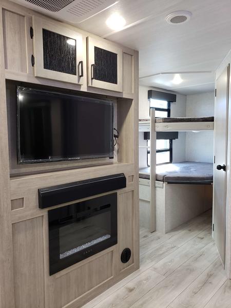 RV rental interior: Living area with TV, fireplace, and bunk beds, all in light wood tones.. East to West Alta 2024