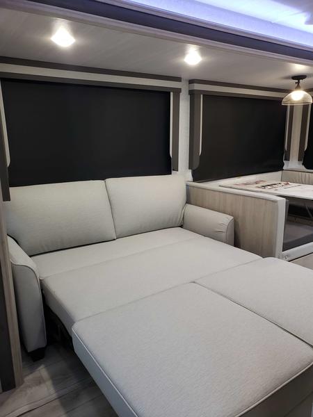 Cozy RV rental interior with a light-colored sofa converting into a bed, alongside blackout shades and a dining area.. East to West Alta 2024