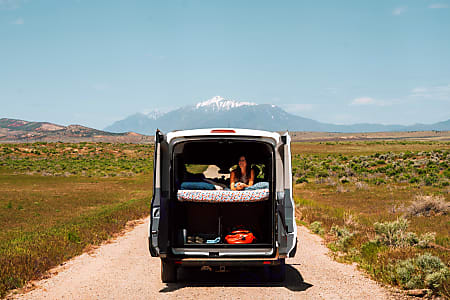 Perfect RV rental for van life! Woman lounging in a camper van with rear doors open, scenic mountain view.. Ford transit 2017