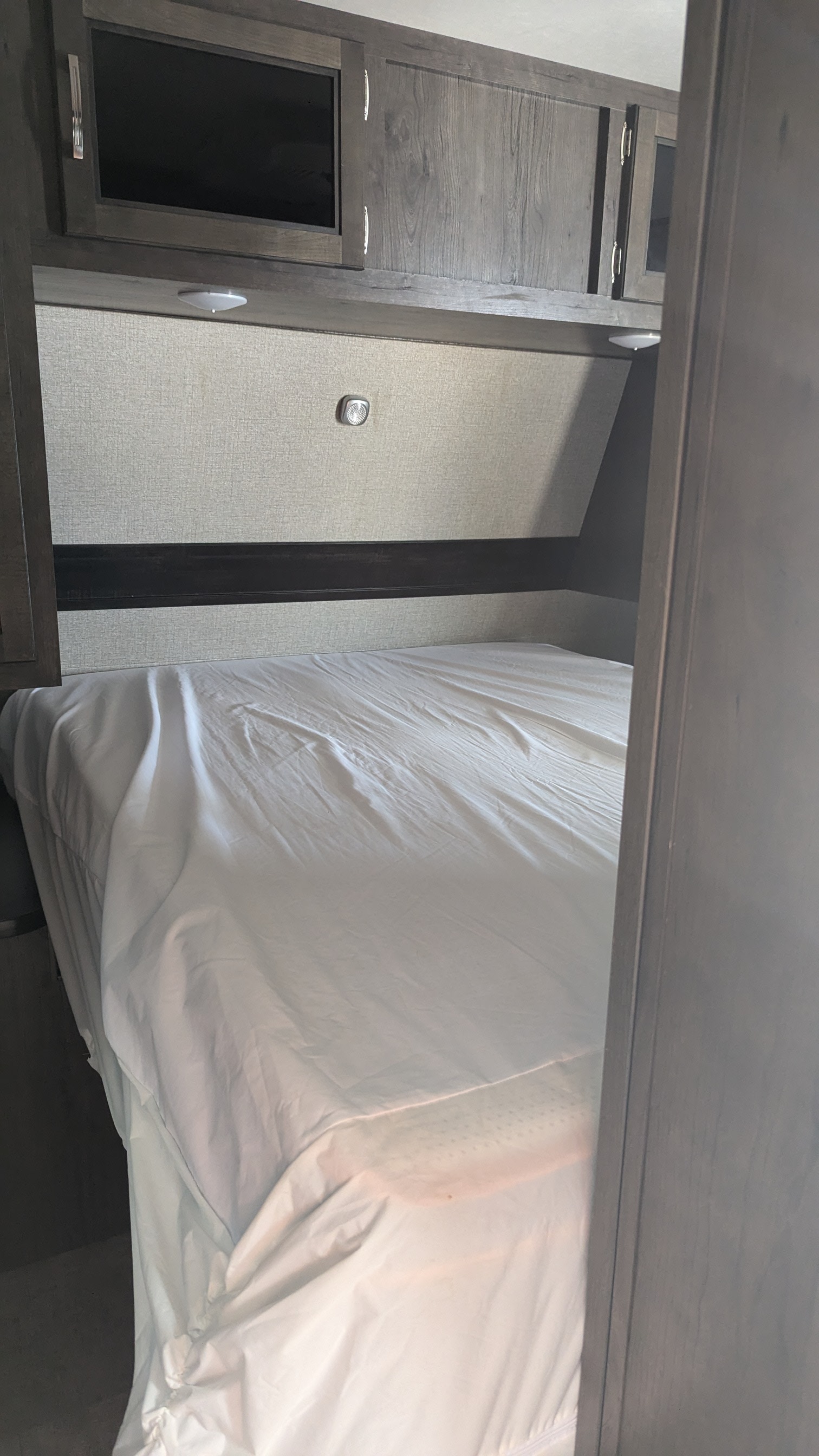 This RV rental bedroom offers a comfortable bed with white sheets, compact overhead cabinets (one with a TV), and built-in lighting.. Jayco Jay Flight 2020