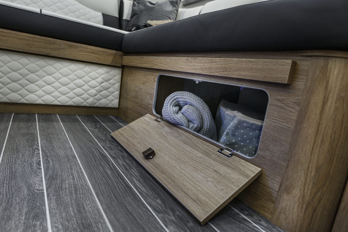 RV rental interior features convenient under-bench storage, revealing a cozy blanket and organized items for comfortable travel.. FIAT RollerTeam 747 2022