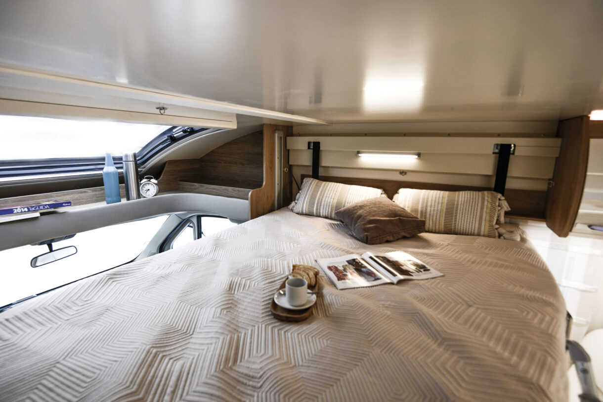 Cozy cab-over bed in an RV rental, with coffee and a magazine for a relaxing morning.. FIAT RollerTeam 747 2022