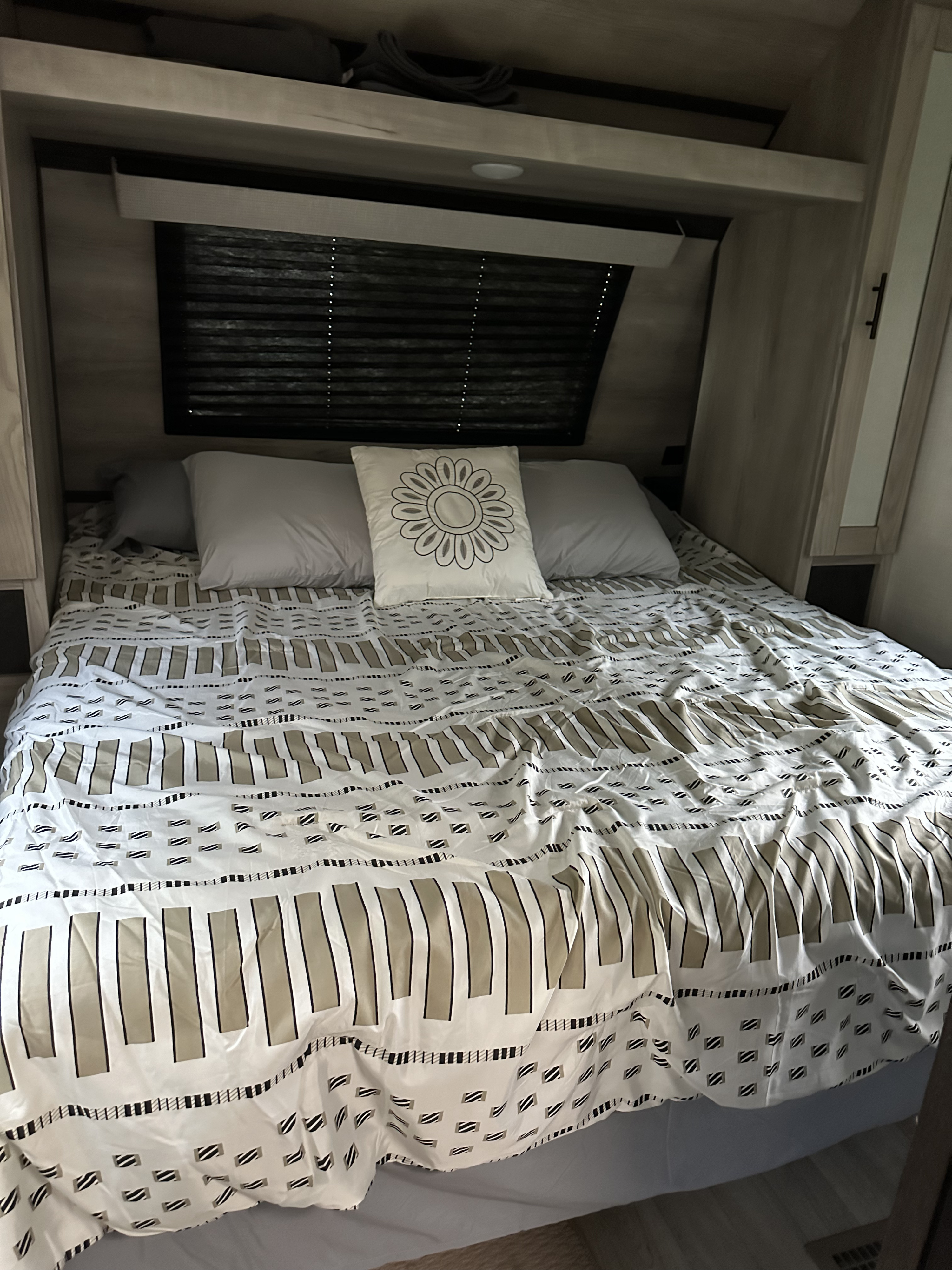 Compact RV rental bedroom featuring a neatly made bed with unique patterned bedding, pillows, and overhead cabinets.. Connect Connect Trailer 2022