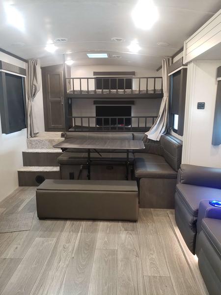 Explore this modern RV rental interior featuring bunk beds, a dinette, and comfortable living area. Great for family trips.. Keystone RV Cougar 2024