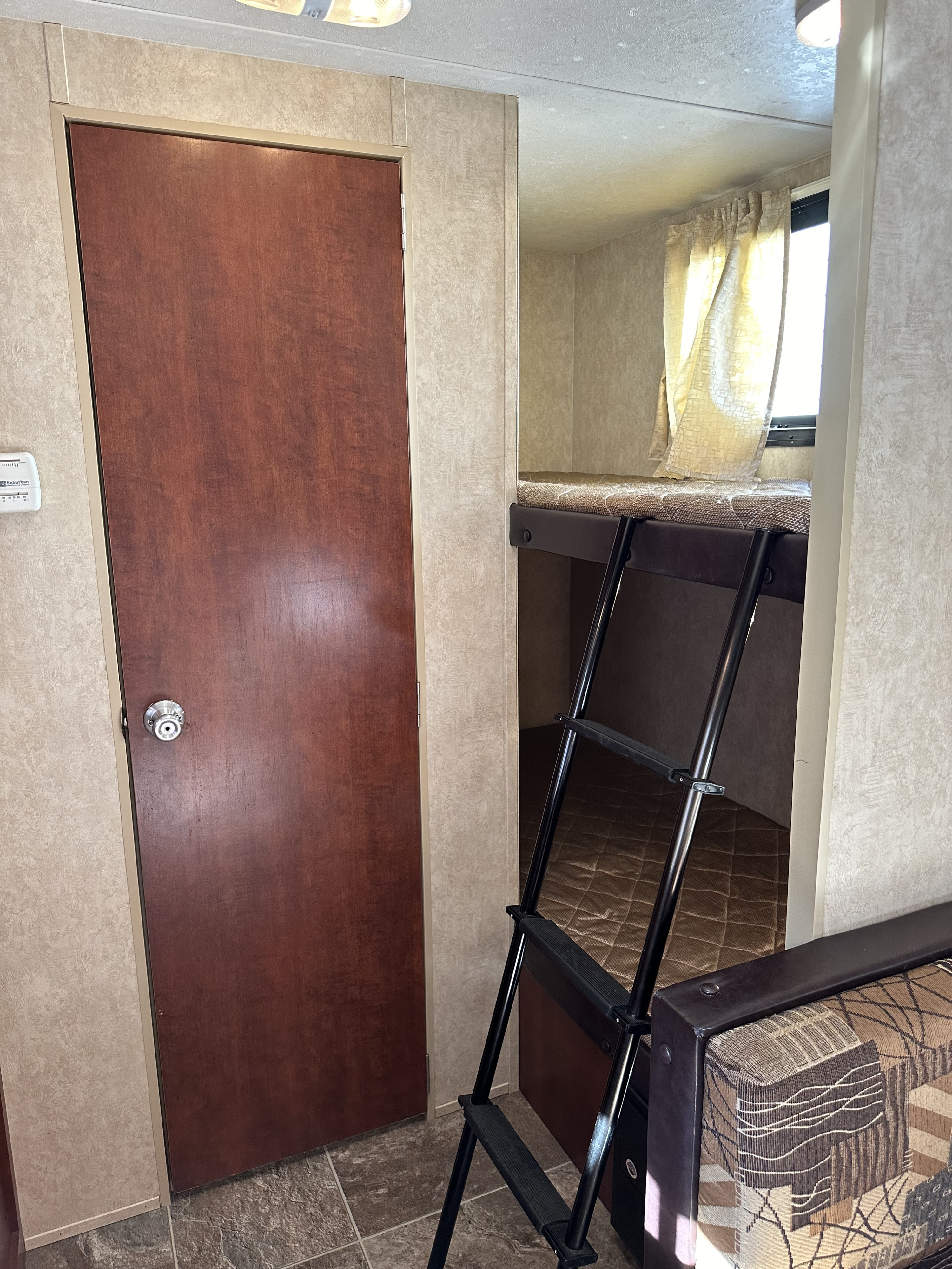 RV rental interior shows a wooden door, thermostat, and bunk beds with a ladder, indicating a cozy, functional space.. Forest River Salem Cruise Lite 2017