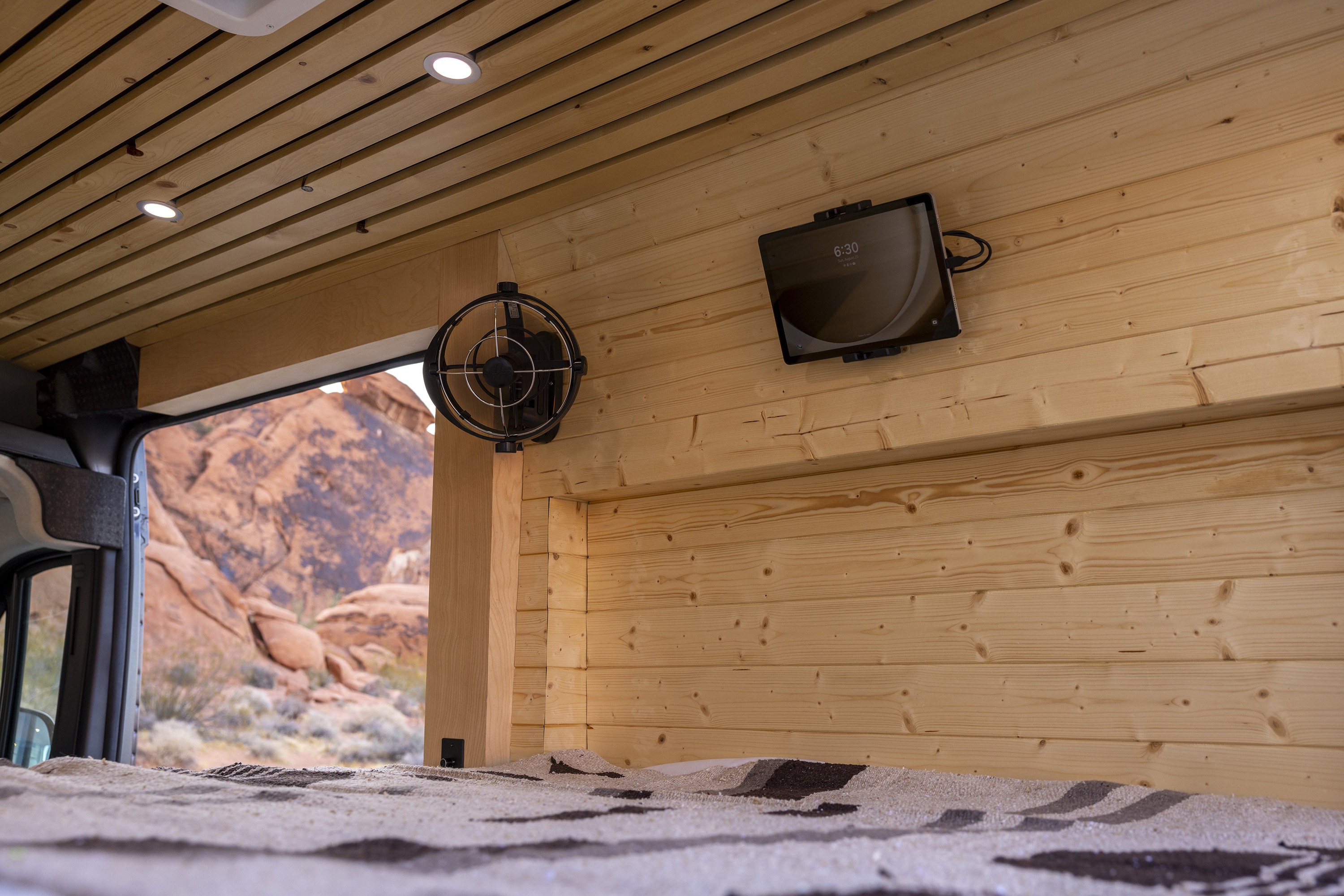 Cozy RV rental interior with wooden walls, fan, tablet, and a stunning desert view outside. Perfect for adventures!. Custom RAM Promaster 2023