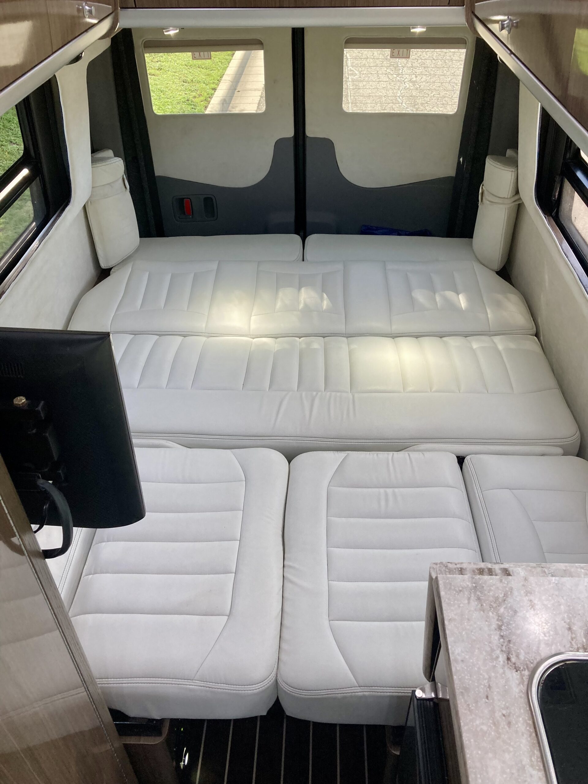 RV rental interior with a white convertible bed/seating arrangement, a monitor on the left, and a small counter/sink.. Airstream Interstate 2018