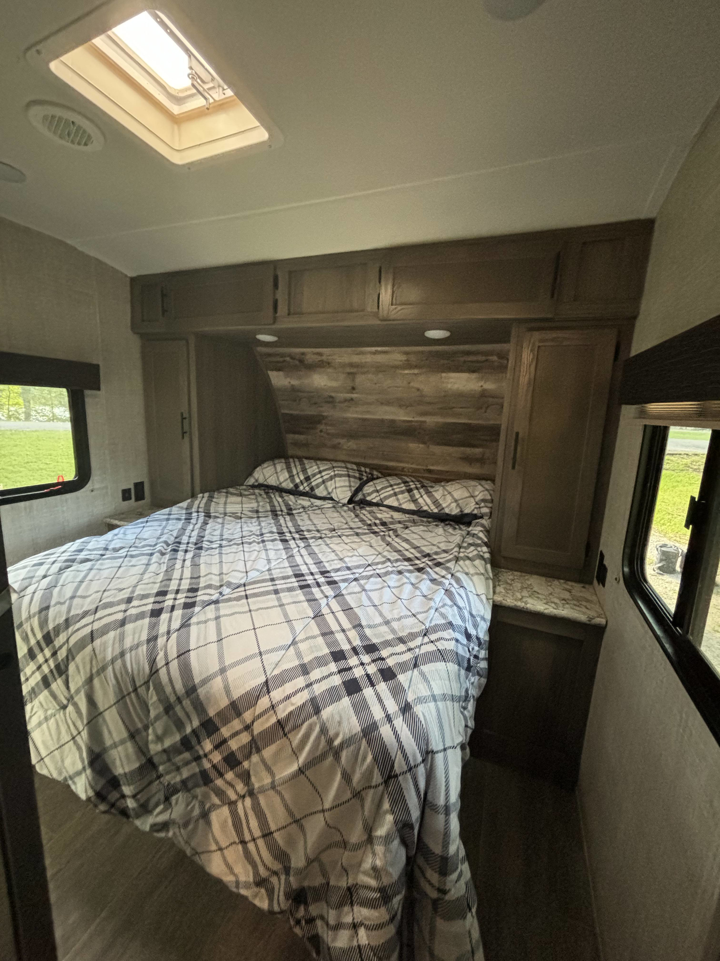 Cozy RV rental bedroom with plaid bedding, wood headboard, overhead cabinets, windows, and a skylight.. Gulf Stream Conquest 2020