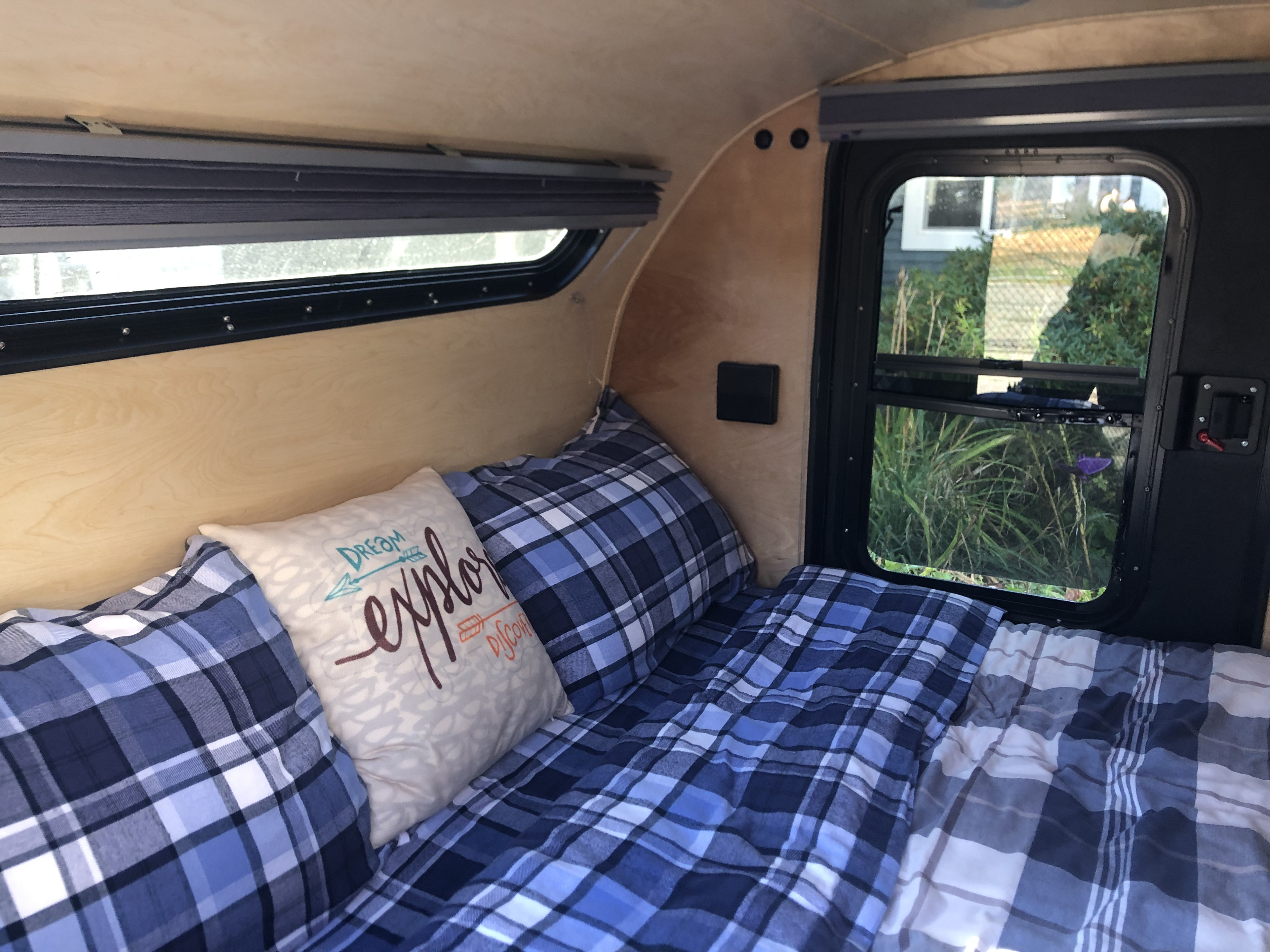 Inviting RV rental sleeping space with blue plaid bedding, a "DREAM EXPLORE DISCOVER" pillow, and scenic windows.. Little Guy Little Guy Trailer 2013