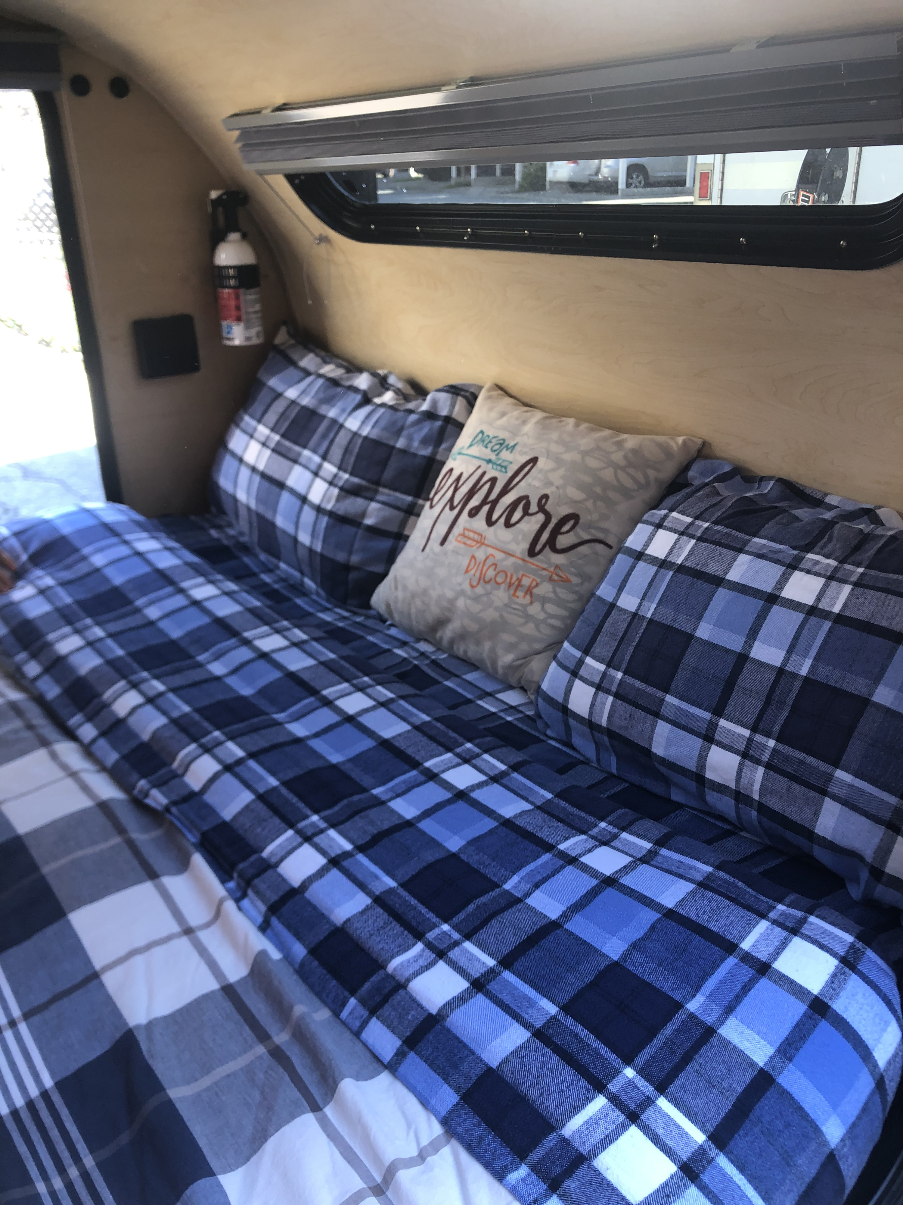 RV rental interior: cozy bed with blue plaid bedding, a window with shades, and a fire extinguisher mounted on the wall.. Little Guy Little Guy Trailer 2013