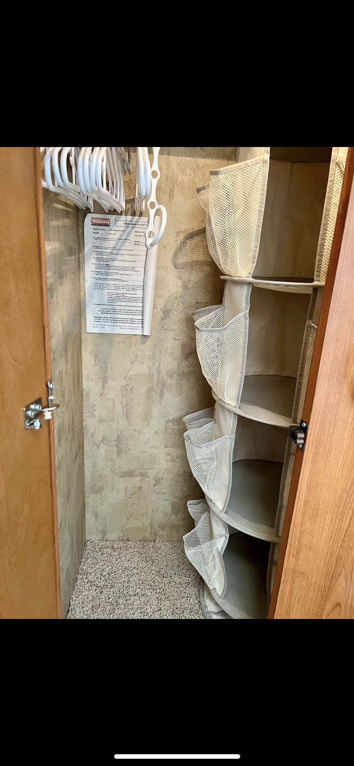 Inside an RV rental closet: multi-tier fabric organizer, white hangers, and a Winnebago info sheet on the wall. Carpeted floor.. Winnebago View 2007