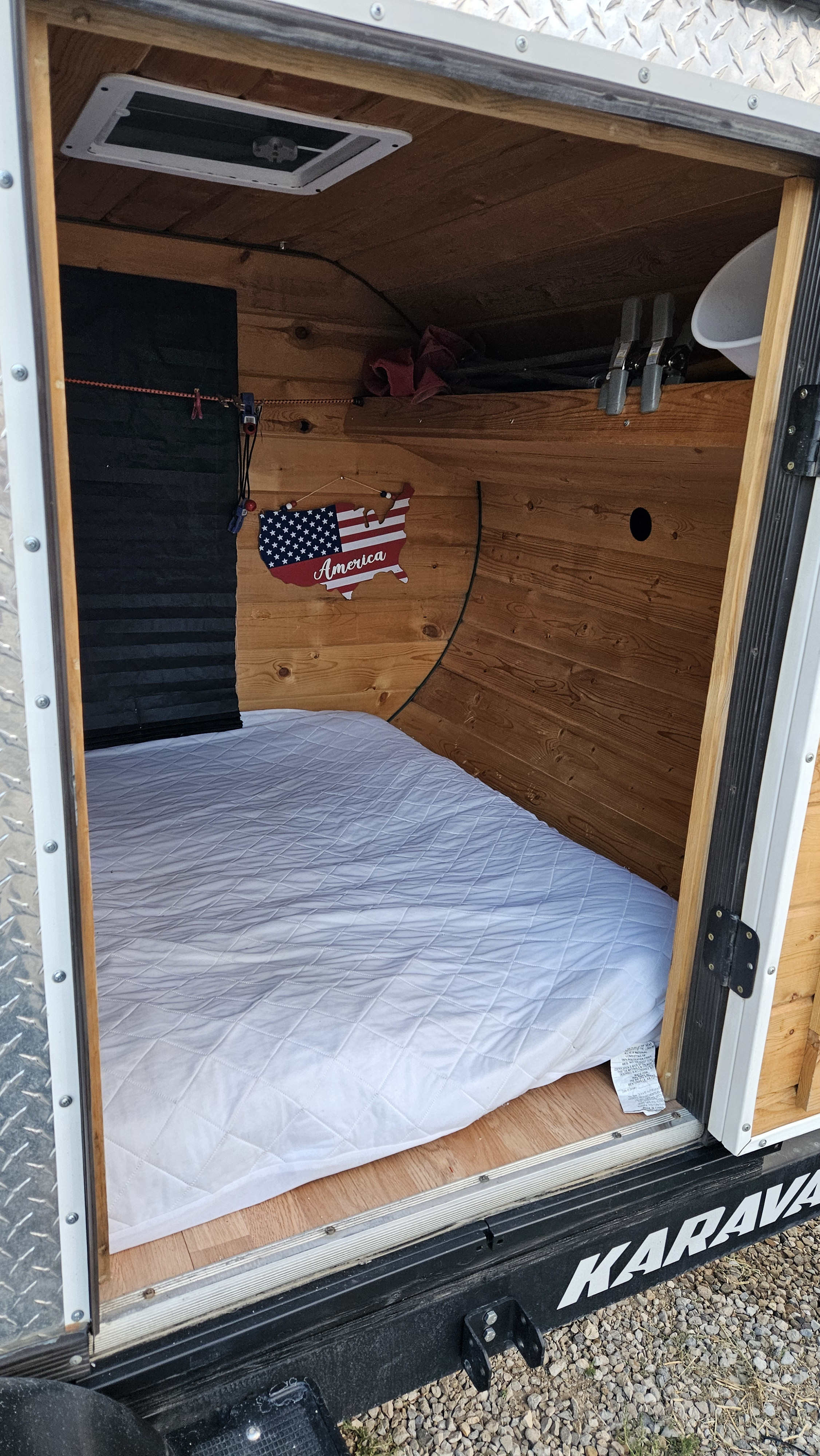 RV rental: Inside a small, wood-paneled camper featuring a comfortable mattress, roof vent, and patriotic decor.. Homemade Teardrop 2020