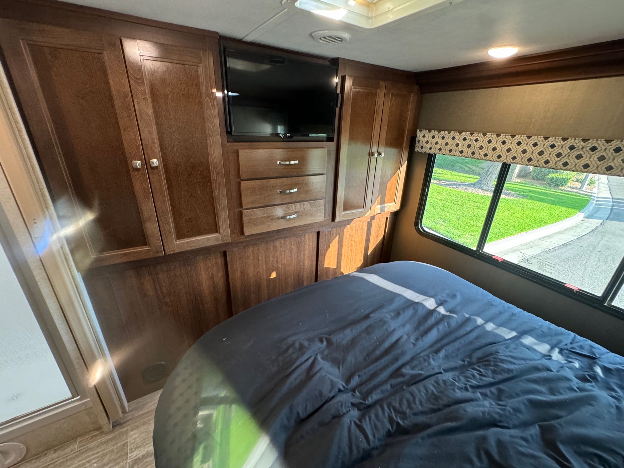 This RV rental bedroom offers a cozy bed, entertainment with a TV, ample wooden storage, and a scenic window view.. Forest River Forester 2019