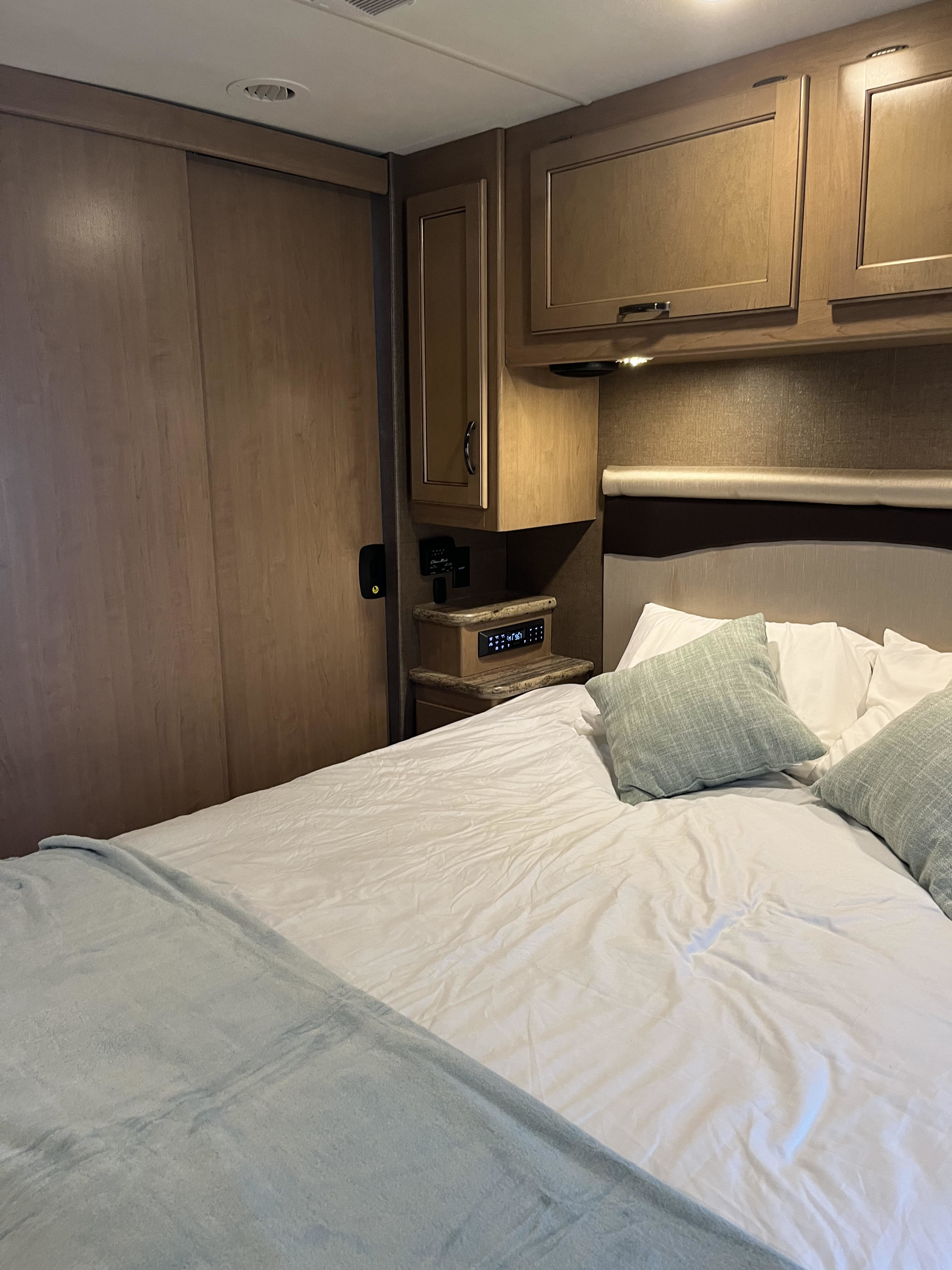 Cozy RV rental bedroom featuring wood cabinetry, sliding doors, a bed with light blue accents, and a smart control panel.. Thor Motor Coach ACE 2018