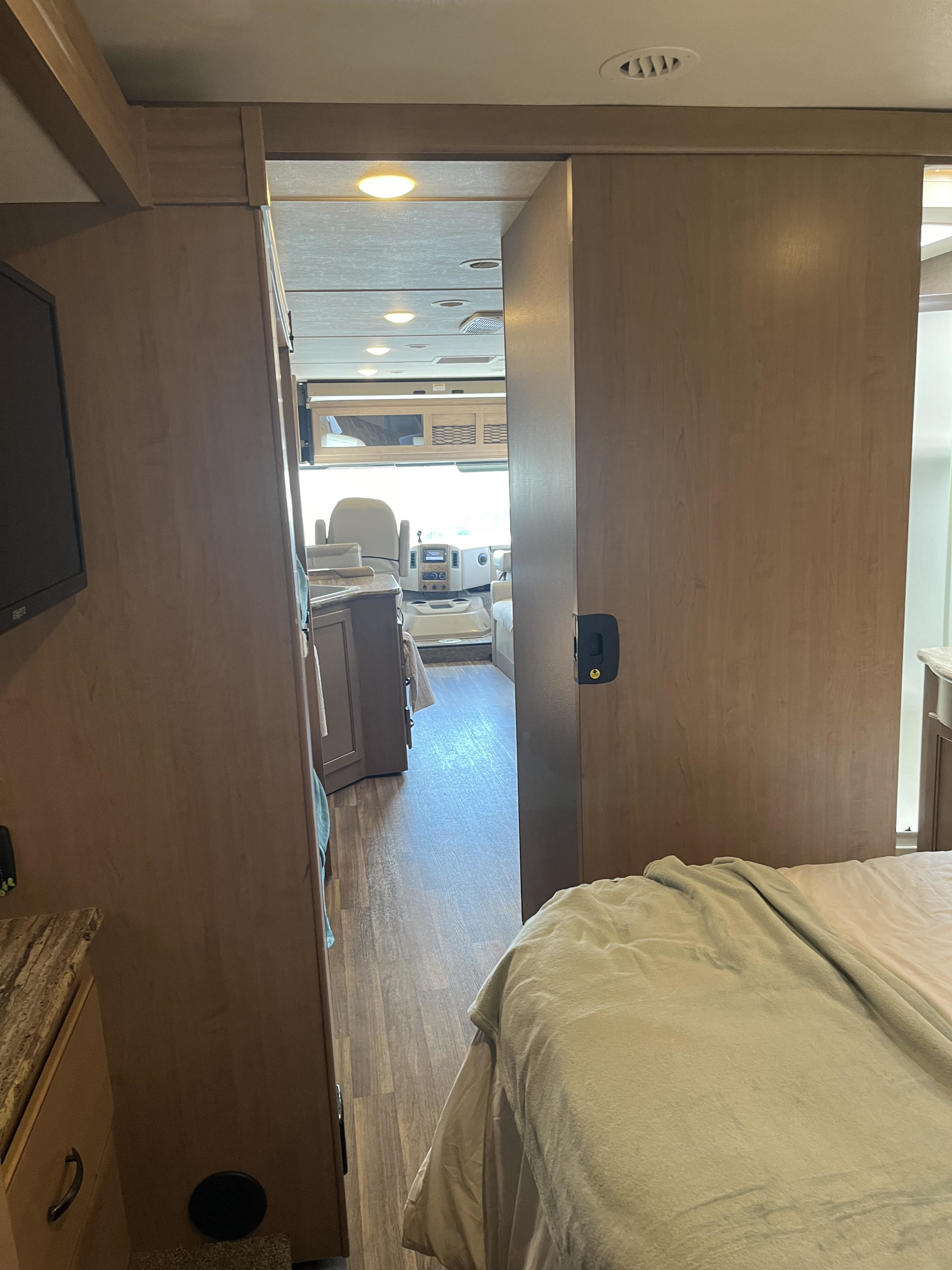 View inside an RV rental, showing the bedroom looking towards the front cockpit area with light wood finishes.. Thor Motor Coach ACE 2018