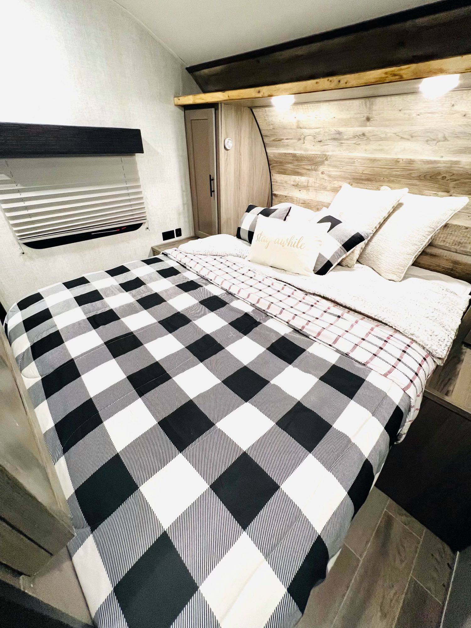 Cozy RV rental bedroom featuring buffalo check bedding, warm wood headboard, and soft lighting for a comfortable stay.. Gulf Stream Gulf Stream 2021
