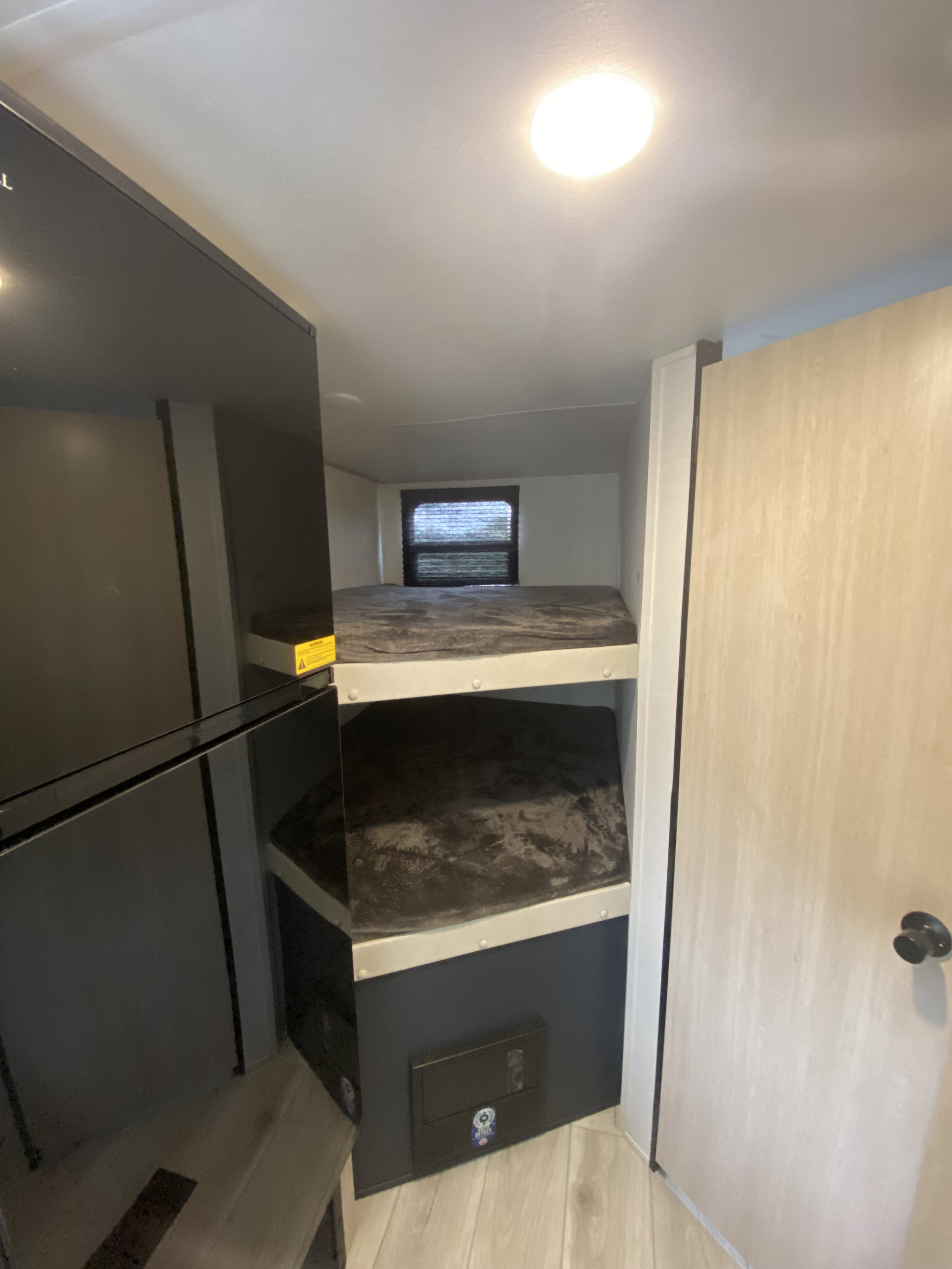 Cozy RV rental interior featuring stacked bunk beds with dark bedding, a large black refrigerator, and an accessible electrical panel.. Prime Time Avenger 2024