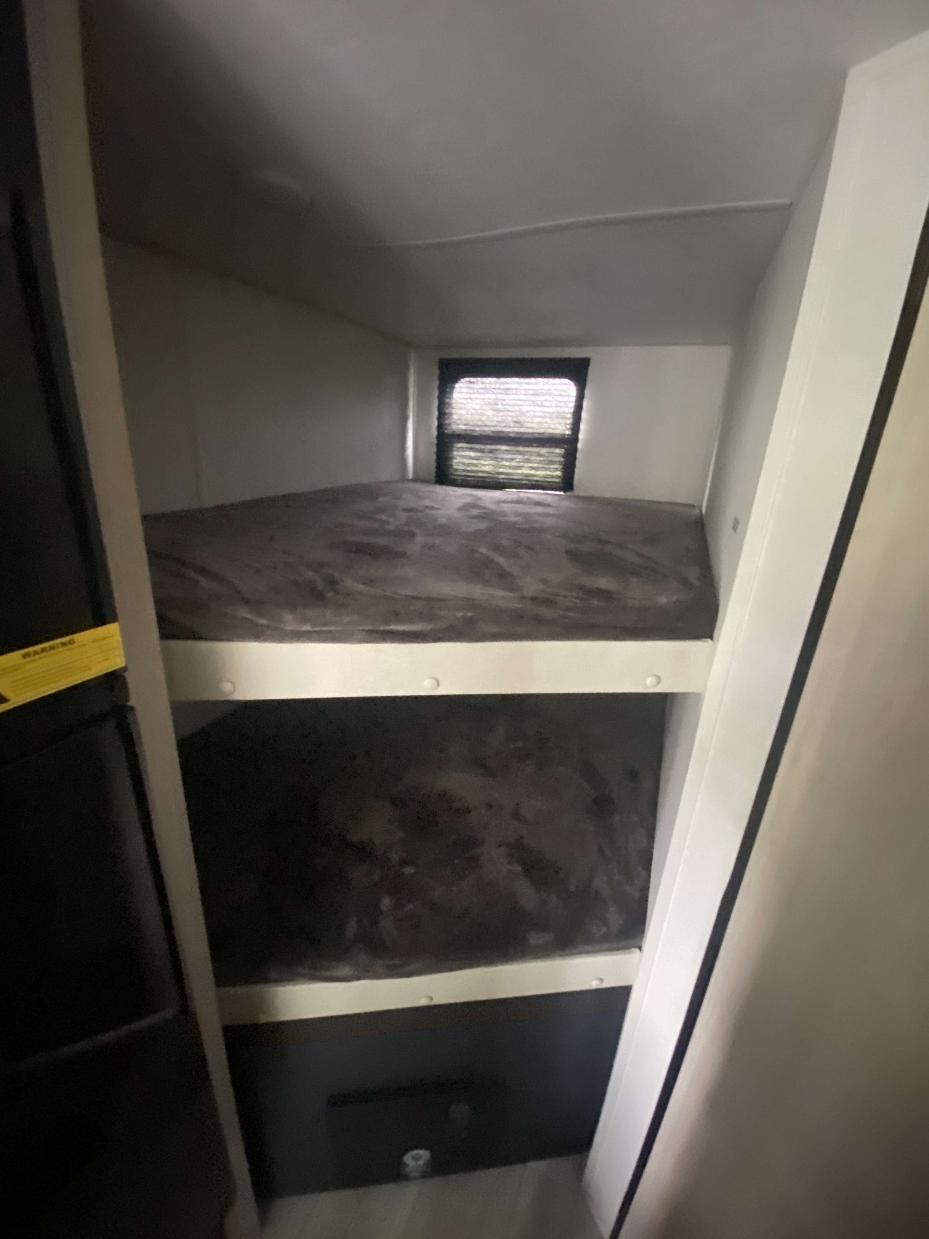 View of two dark-colored bunk beds inside a compact RV rental, with a small window at the top bunk's end.. Prime Time Avenger 2024