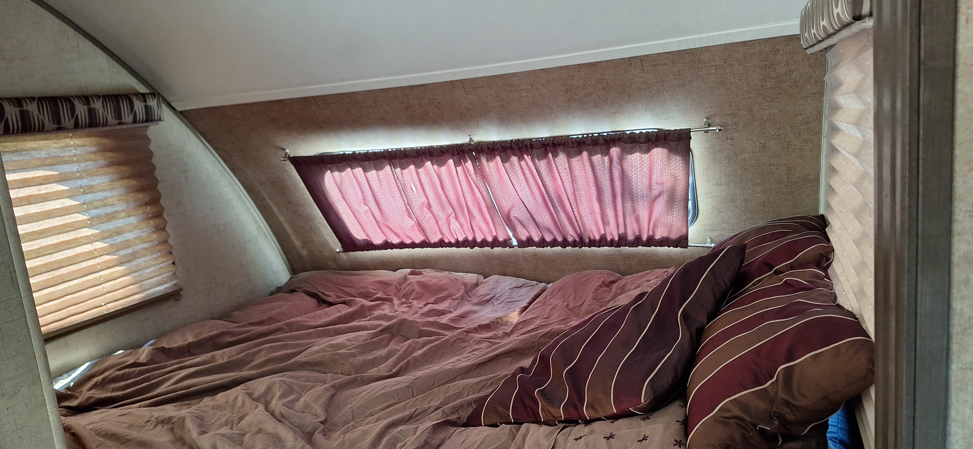 Cozy RV rental bedroom with a bed, window blinds, and a small privacy curtain over an angled window.. Forest River Rpod 2016