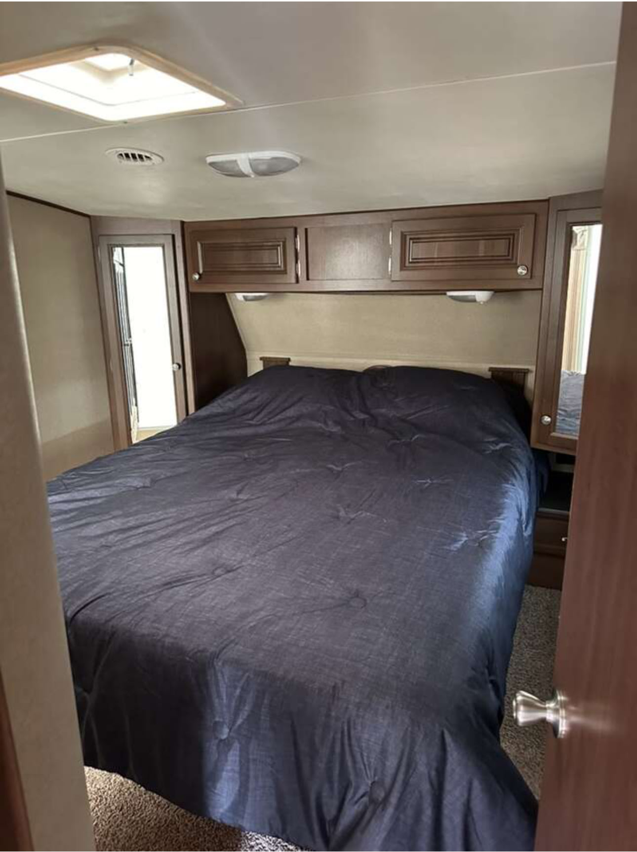 RV rental bedroom: a cozy interior featuring a bed with dark comforter, overhead cabinets, skylight, and mirrored closet.. Denali Denali Fifth Wheel 2014