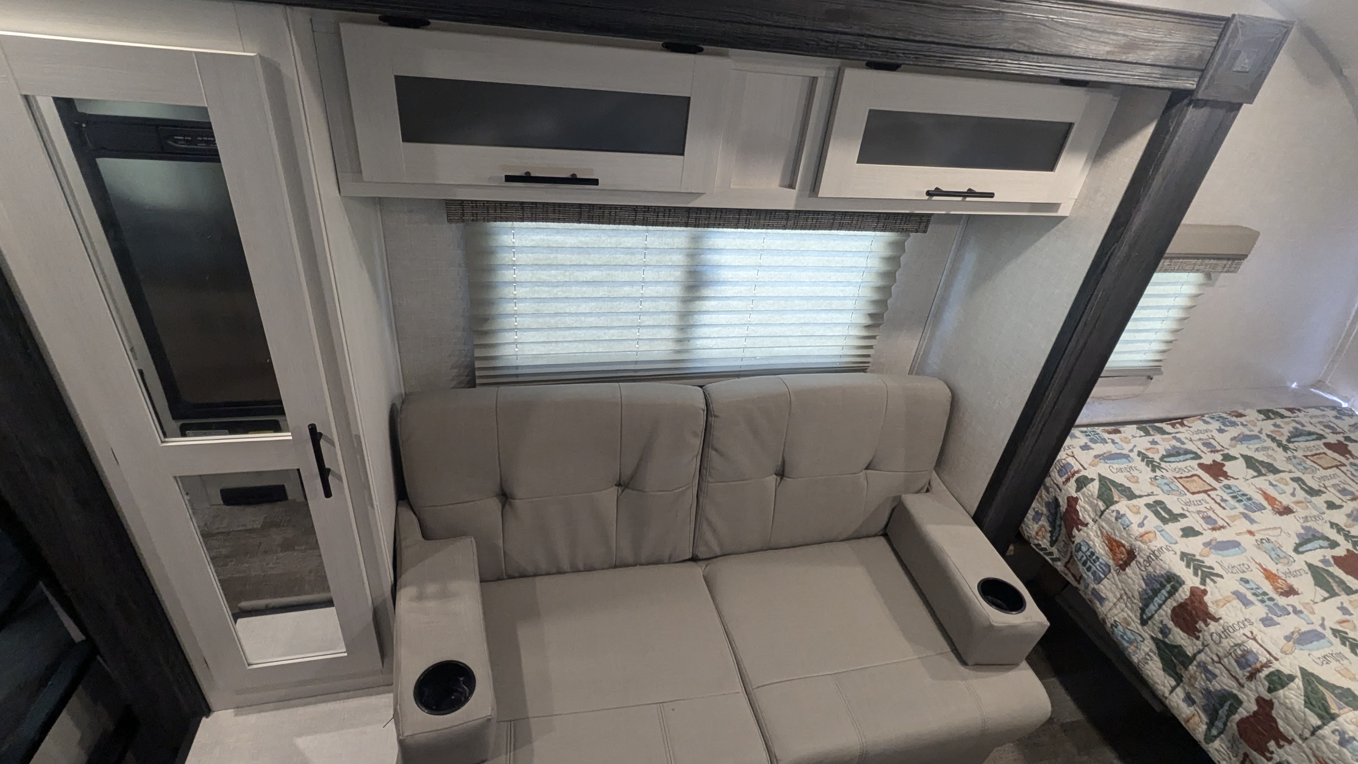 Inside a comfortable RV rental: sofa with cup holders, overhead cabinets, and a bed with a nature-themed quilt.. R-Pod R-Pod Trailer 2022