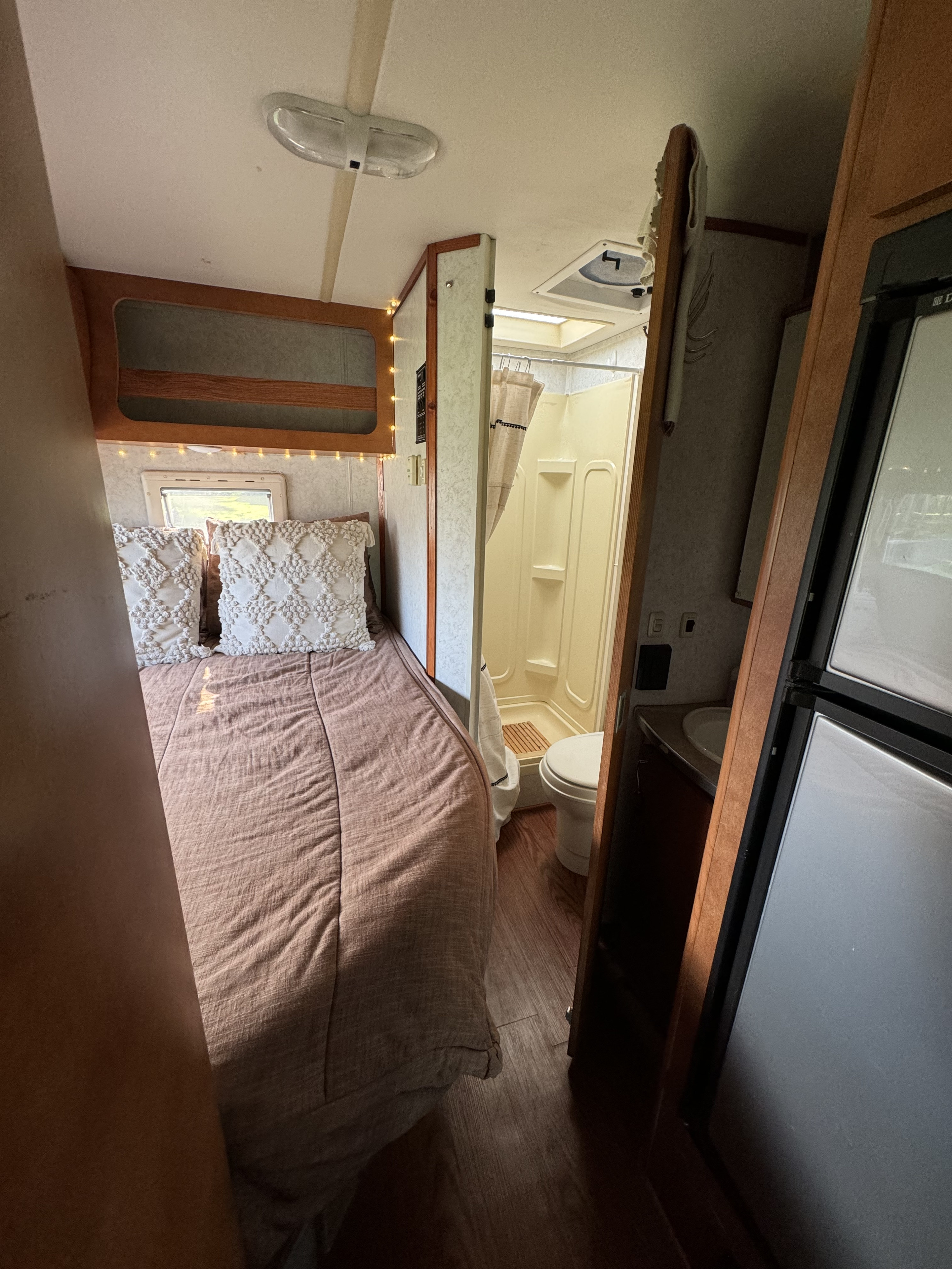 RV rental interior: cozy bedroom with decorative pillows, string lights, plus compact bathroom & fridge.. Gulf Stream Vista Cruiser 2007