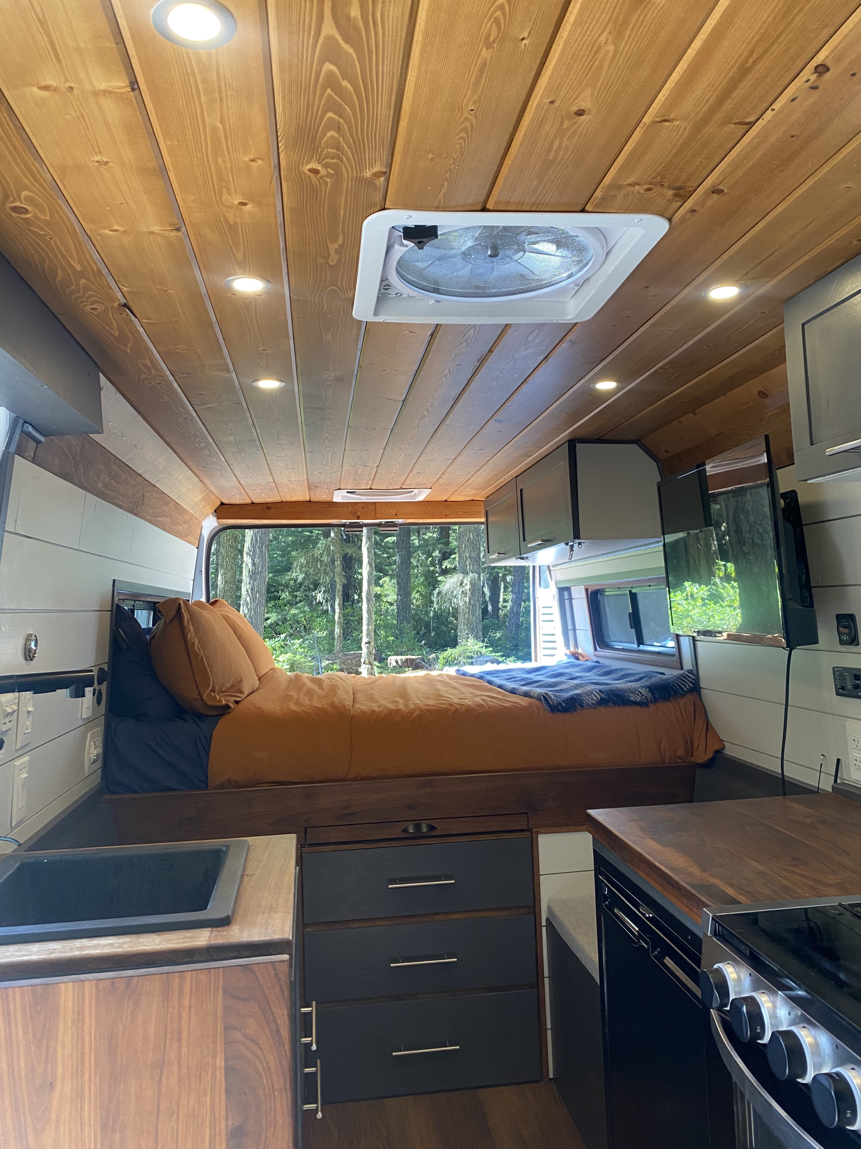 Cozy RV rental interior with wooden ceiling, bed, kitchenette, and forest view, perfect for an adventure.. Dodge Ram 3500 2020