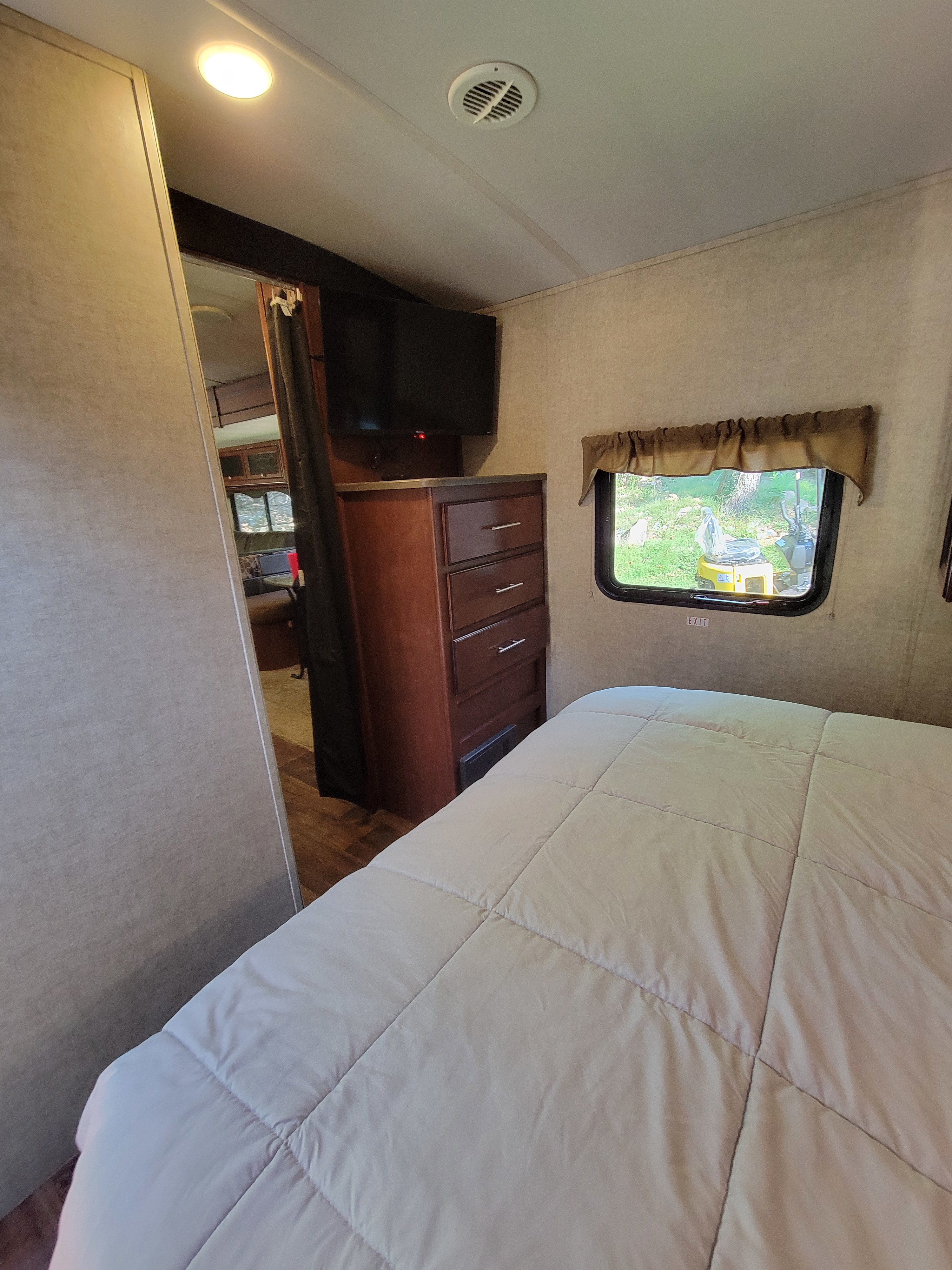 Inside an RV rental bedroom with a comfy bed, wall-mounted TV, dresser, and window. A practical, compact travel space.. Heartland RVs Wilderness 2015