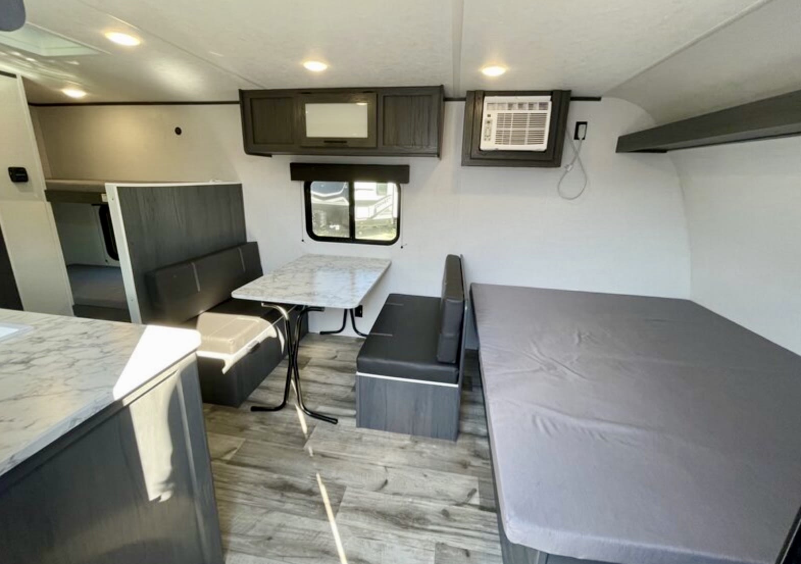 This rv rental interior features a dinette with table, a bed area, overhead storage, AC unit, and bunk beds.. 4YDTATG12S8920028 Dutchmen Aspen Trail 17BH 2025