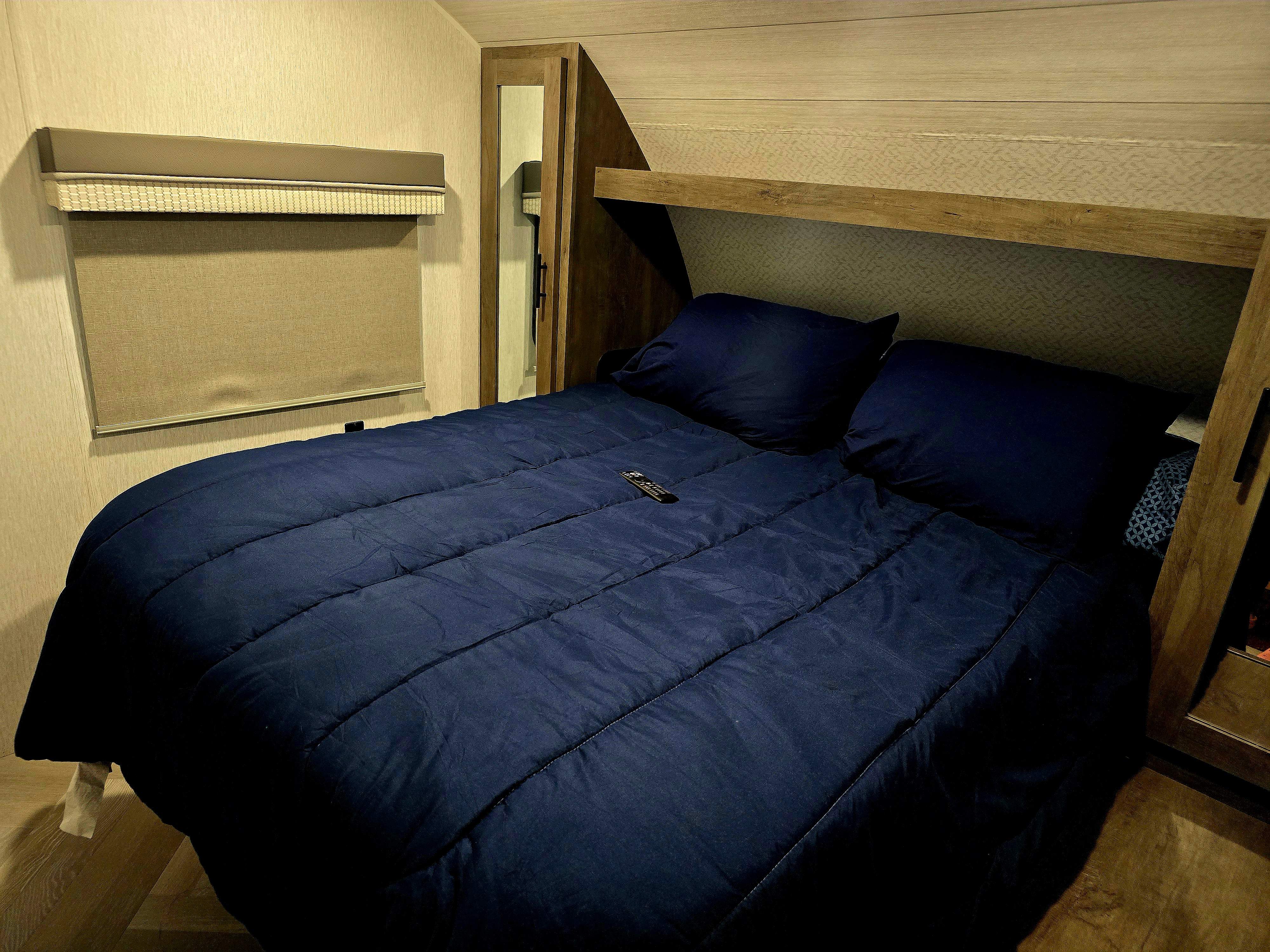 Comfortable RV rental bedroom with a large navy bed, window blinds, and practical built-in wood shelving.. Forest River Salem Cruise Lite 2022